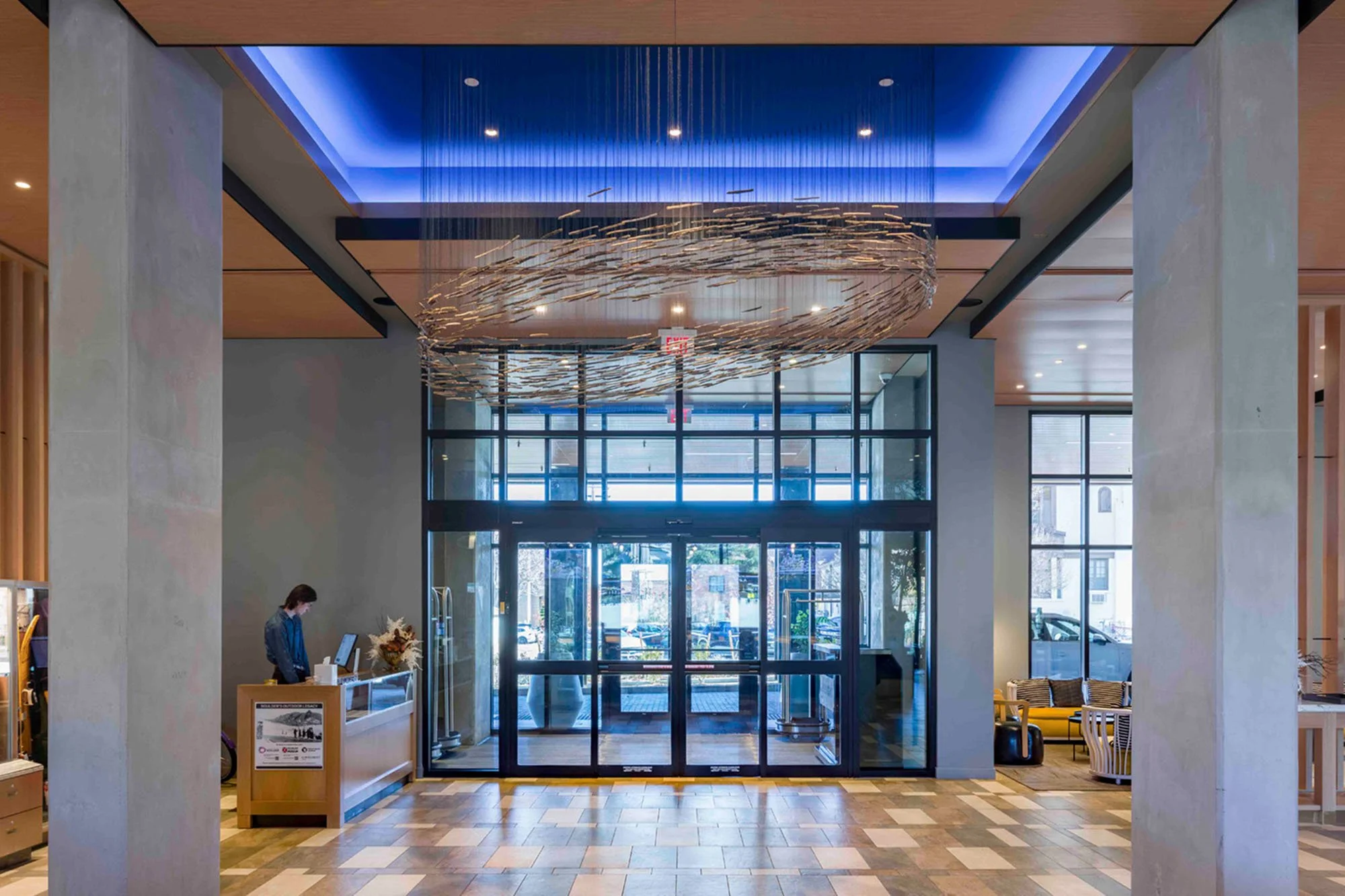A large-scale aerial sculpture titled 'Schooling Possibility' by Theresa Clowes, featuring 2,500 suspended cottonwood sticks arranged to mimic the fluid movement of a school of fish, installed at the Limelight Hotel in Boulder."