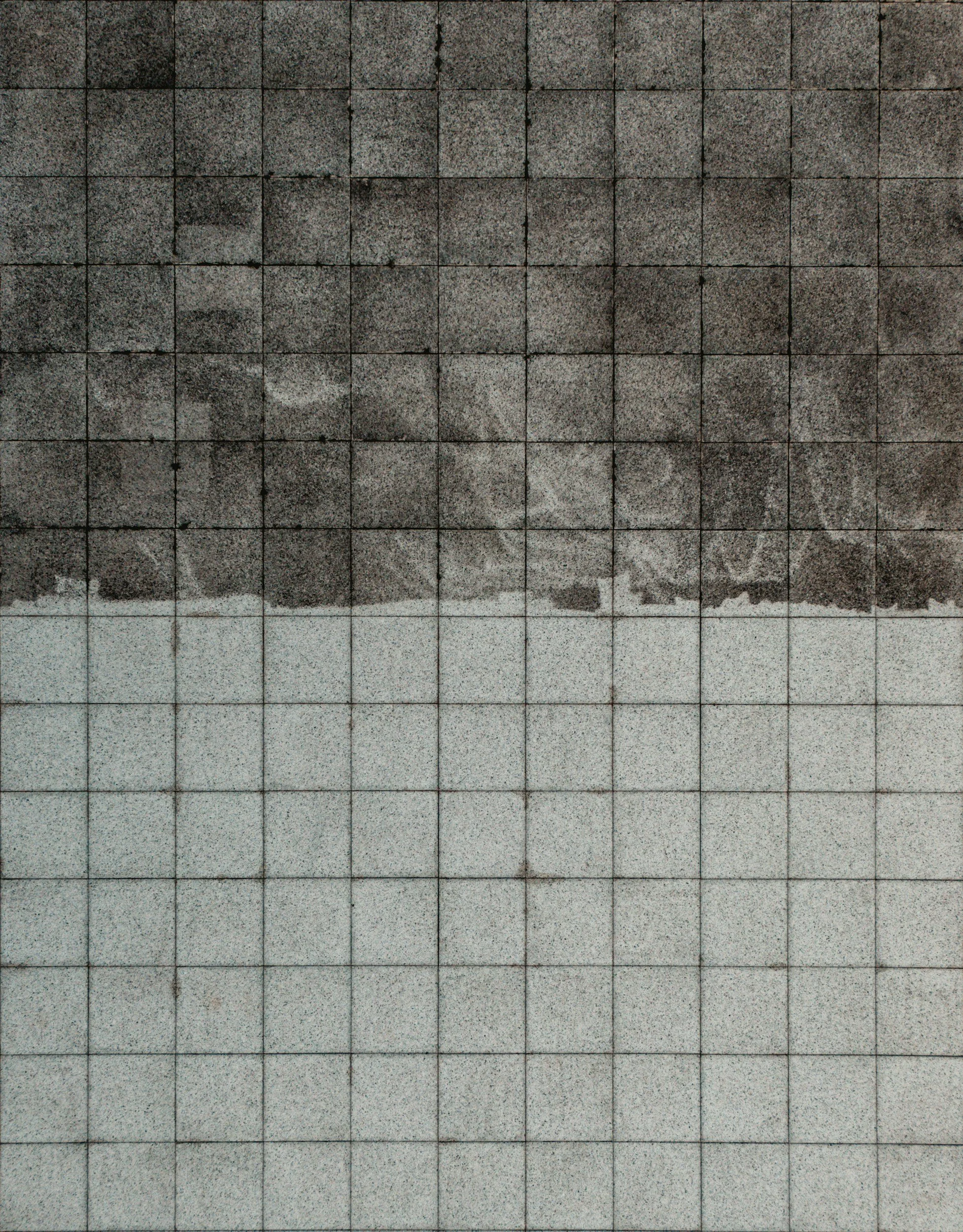 A wall composed of square tiles, with the upper section of dark gray tiles and the lower section of light gray tiles.