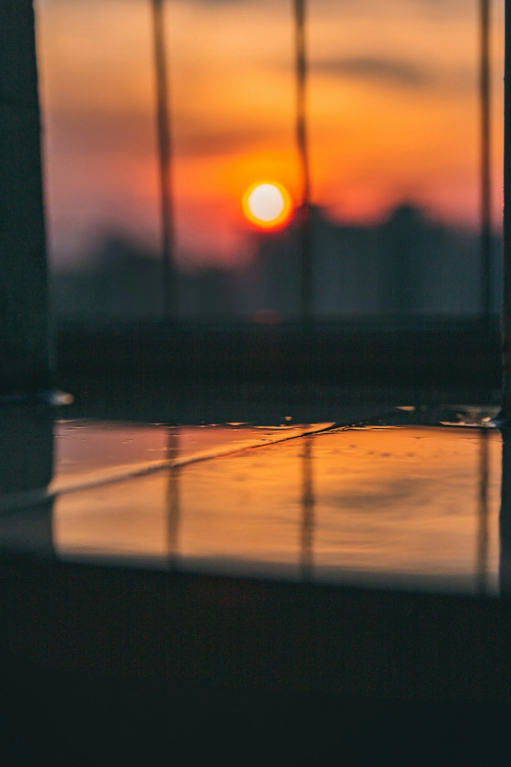 Sunset view through a window with metal bars, reflection on the surface below.