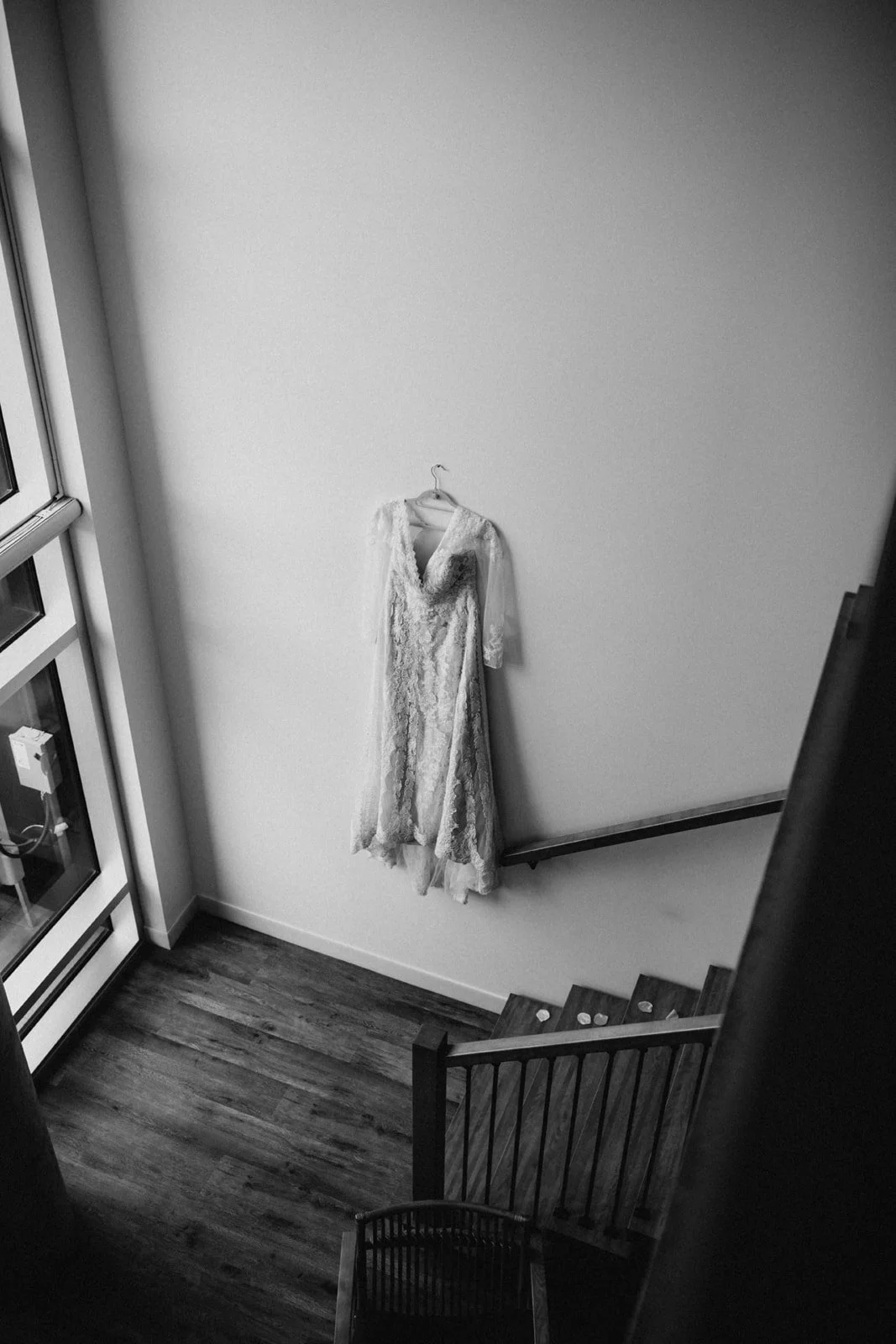 A wedding dress hanging on a wall next to a staircase in a modern interior space.