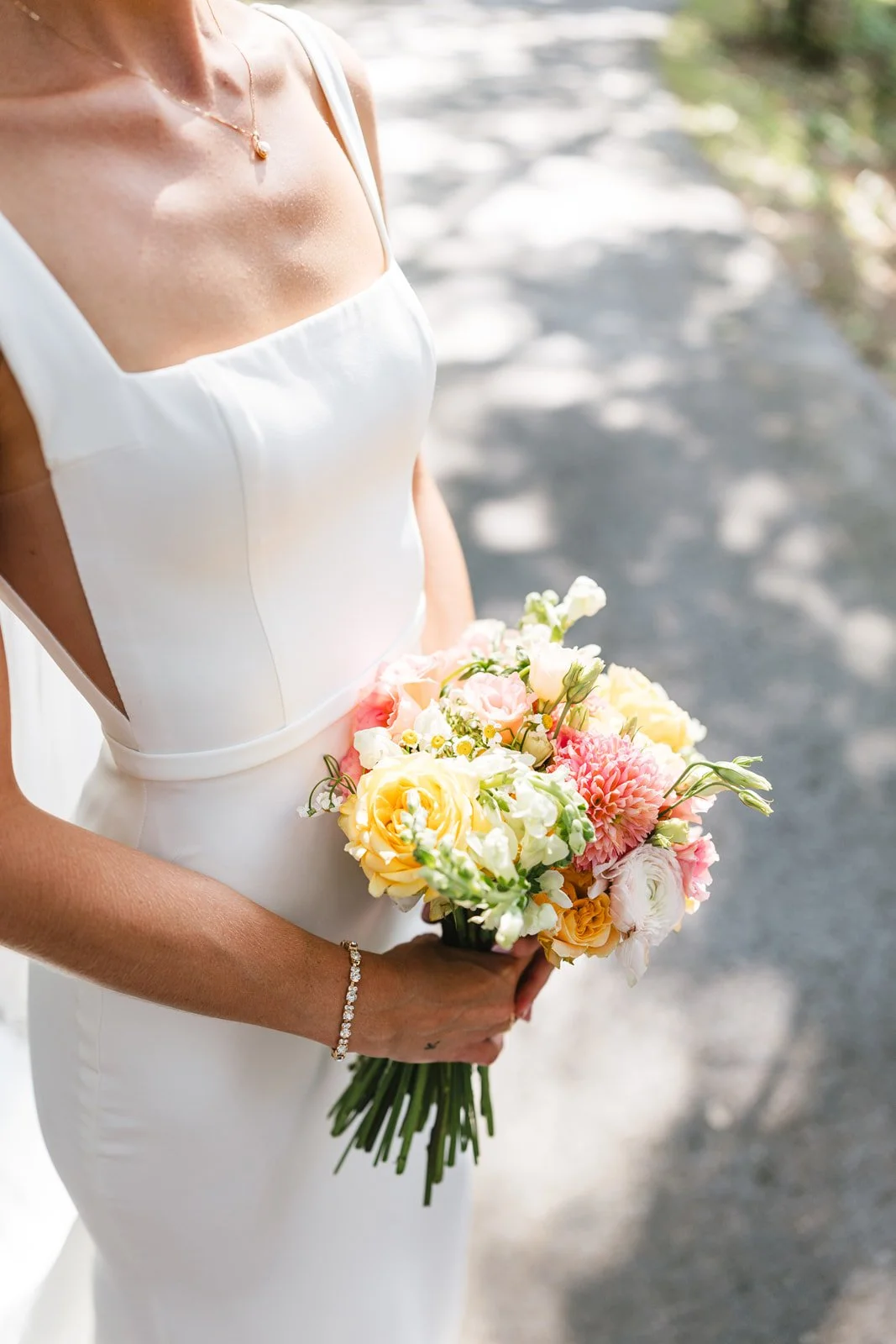 A woman in a white dress holding a bouquet of pastel-colored flowers outdoors.