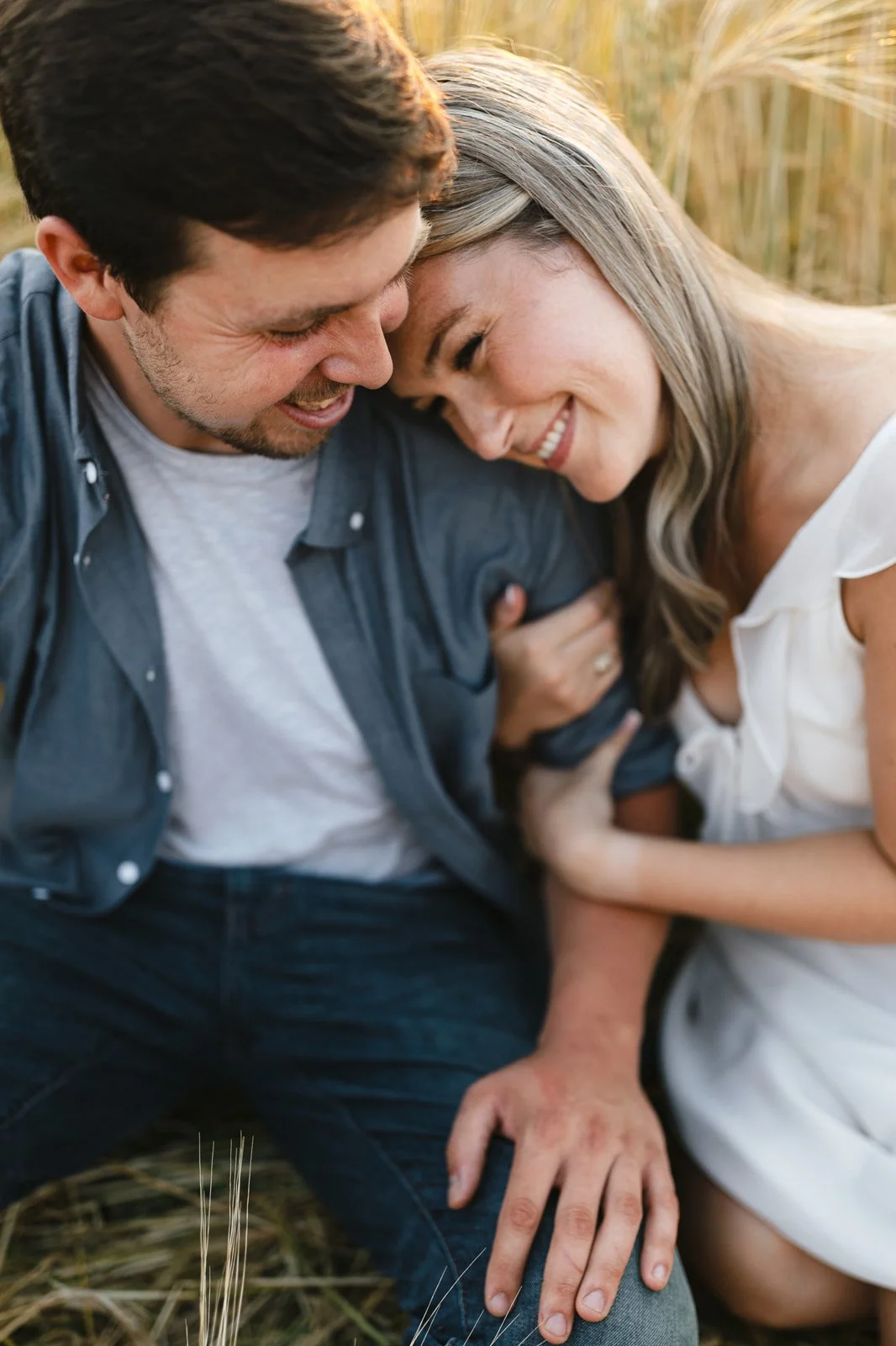 A happy couple sharing a joyful moment outdoors in a field at sunset, close-up with their foreheads touching and smiling