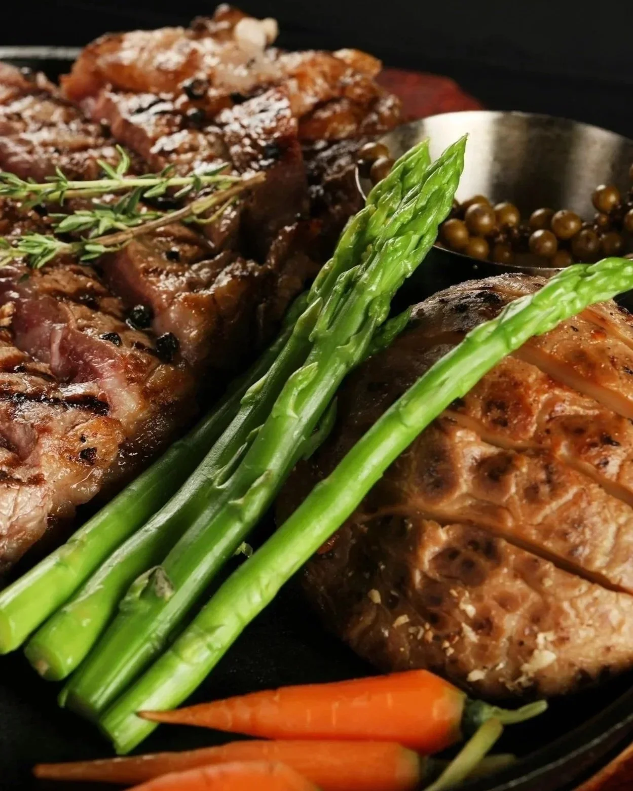 Cooked steak with grilled asparagus, baby carrots, and a sprig of thyme.