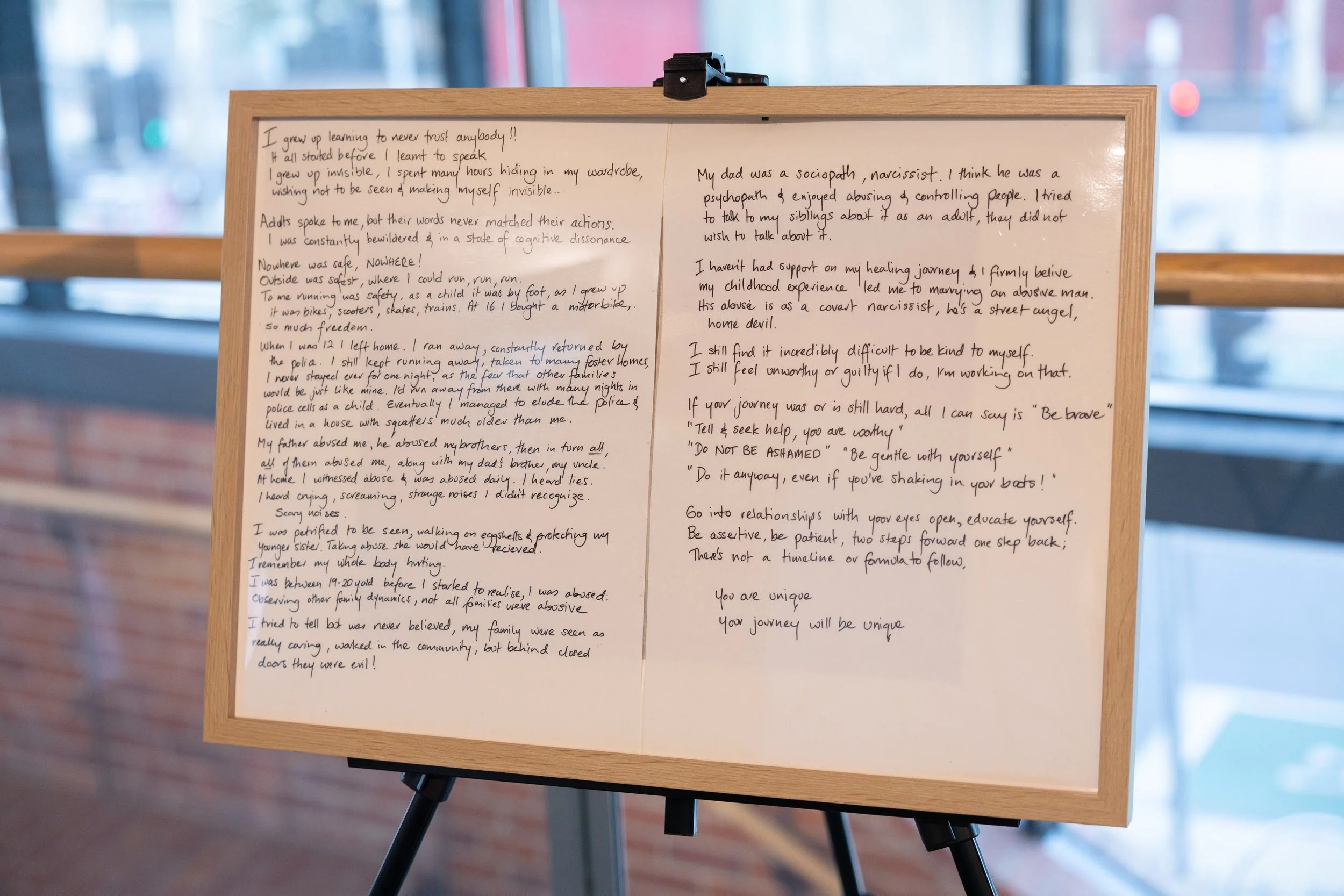 A whiteboard with handwritten notes and reflections about overcoming abuse, personal growth, and advice for others, placed on a stand in front of a large window with a city street outside.