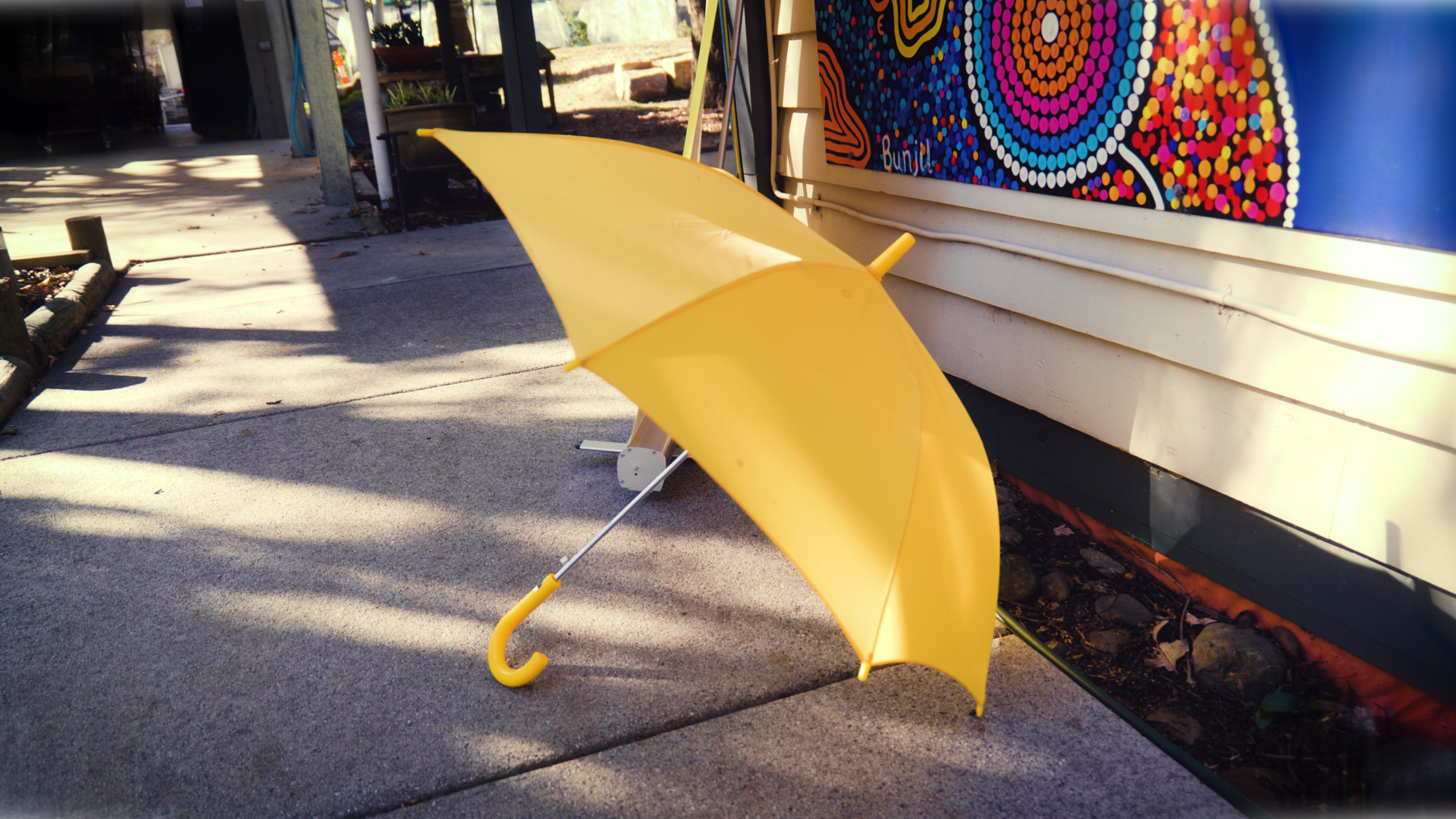 A yellow umbrella resting on the sidewalk near an exterior wall with a colorful dot-patterned artwork.