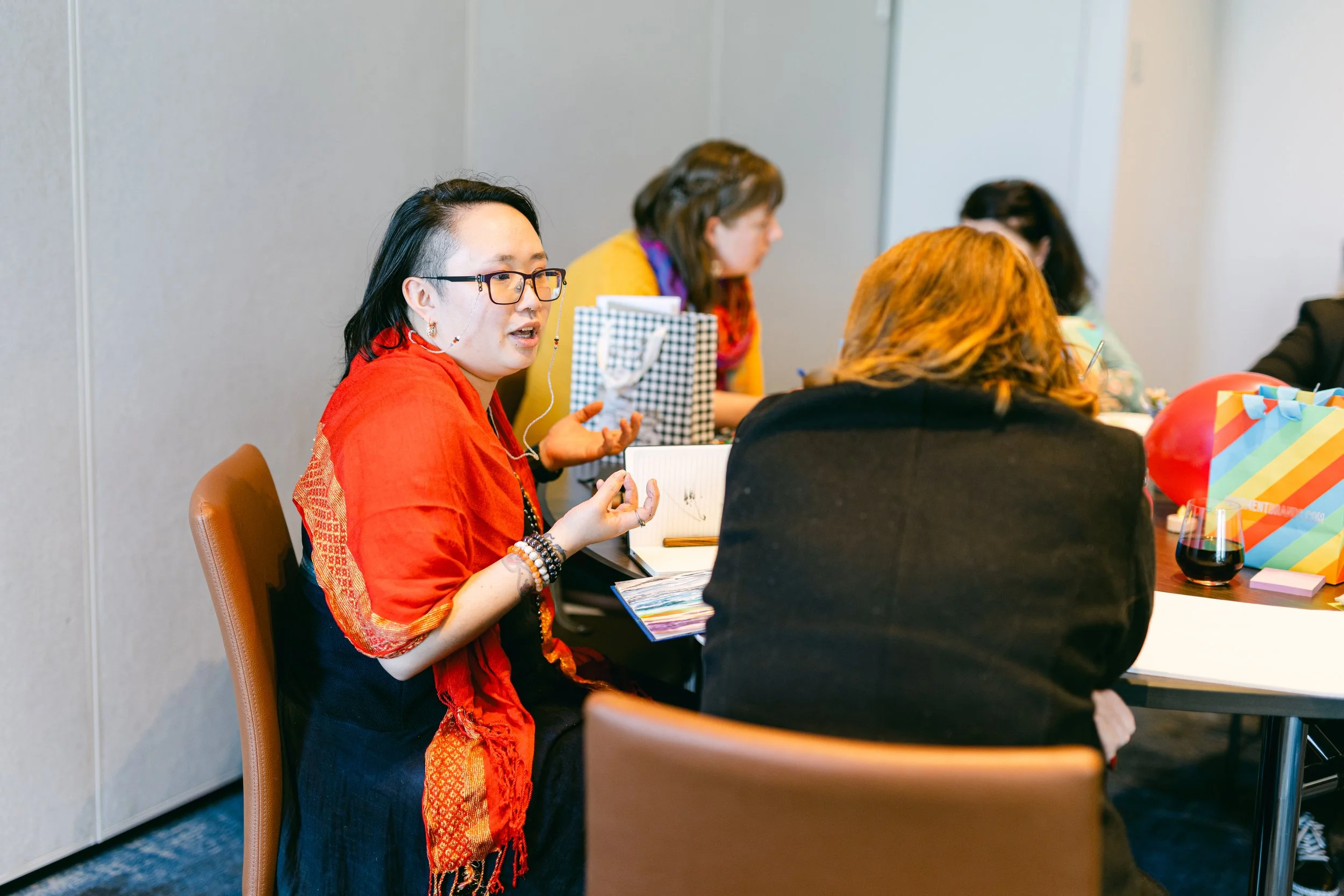 A group of women seated around a table engaged in conversation, with various items and decorations on the table.