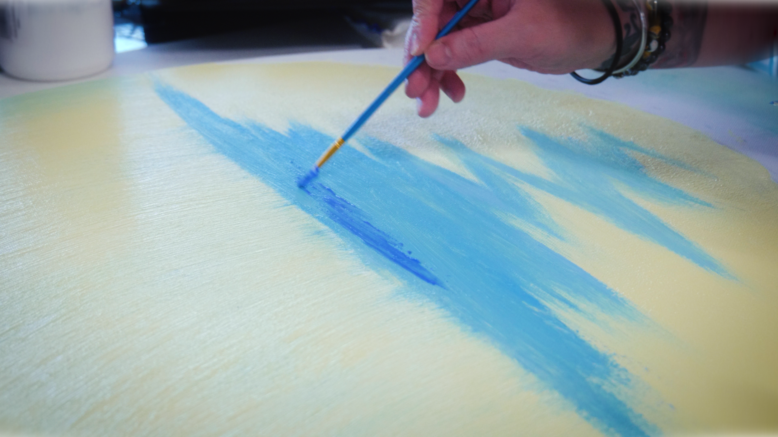 Person painting with blue paint on yellow surface, holding a paintbrush.