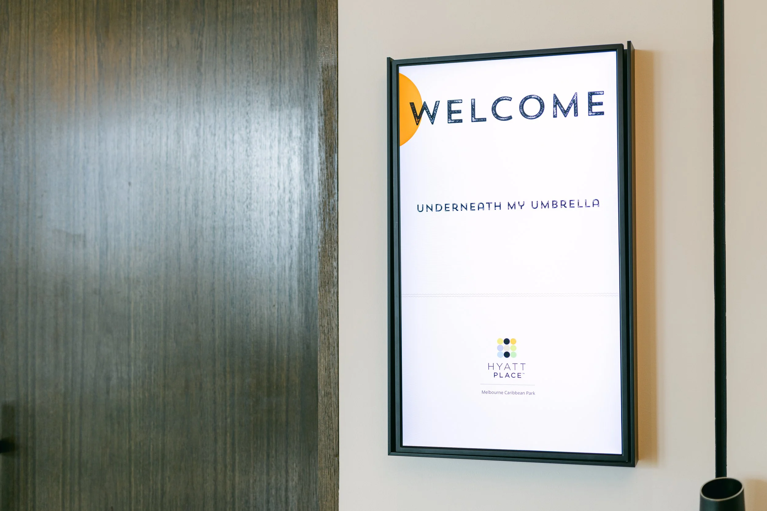 A digital welcome sign displaying 'WELCOME' and 'UNDERNEATH MY UMBRELLA' at Hyatt Place, Melbourne Caribbean Park.