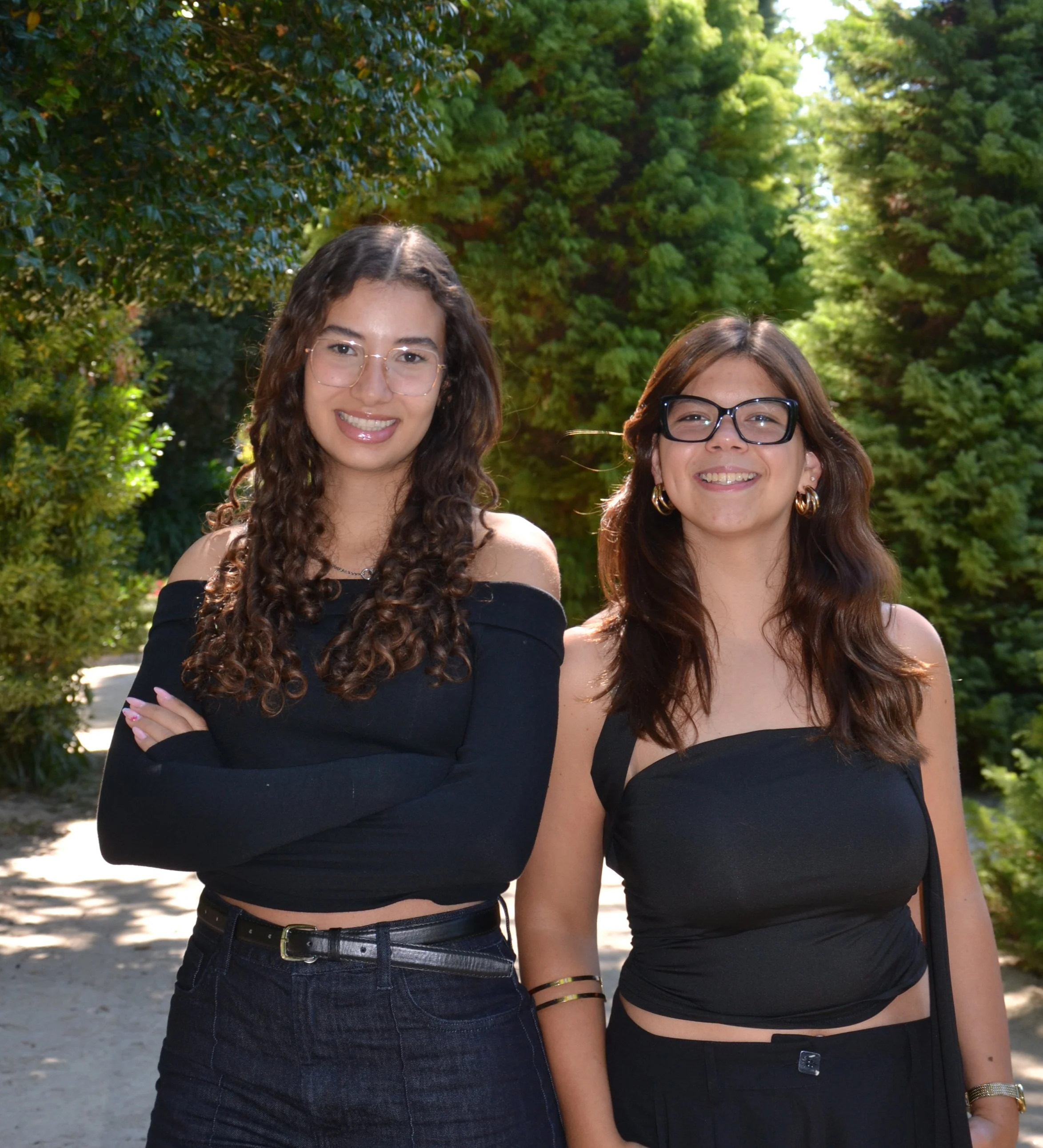 Duas jovens mulheres sorrindo ao ar livre com árvores ao fundo.