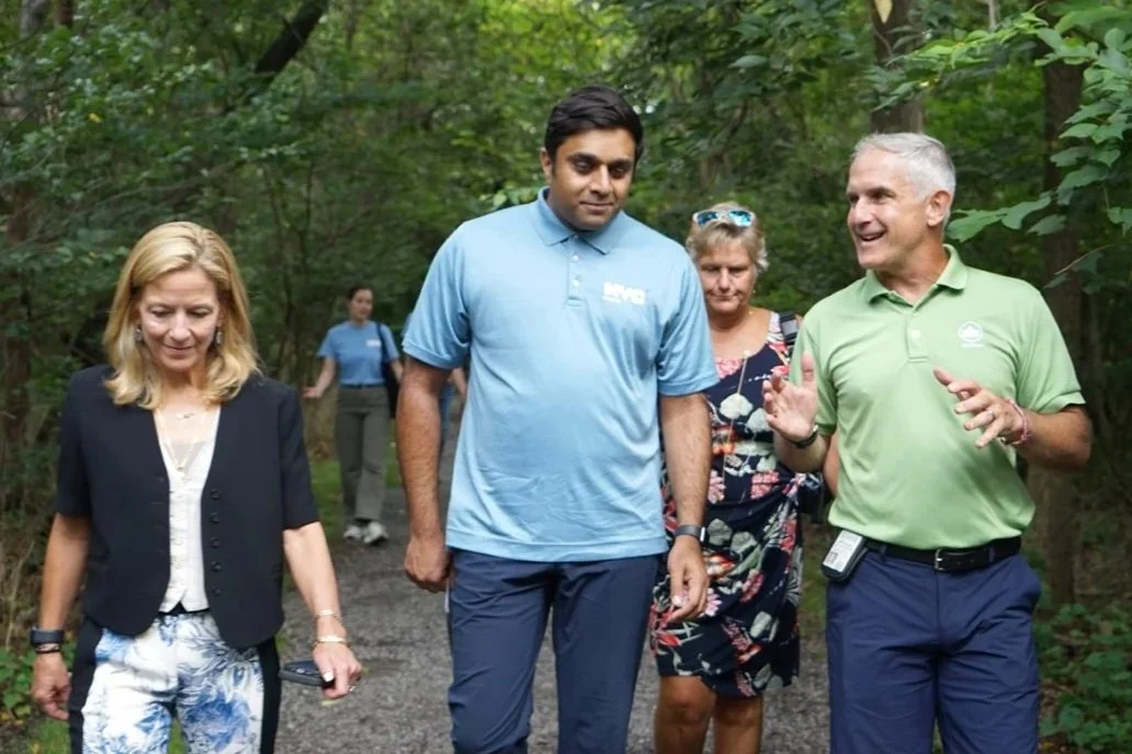 A group of people  with Ashwin Vasan central walking and talking on a forest path, engaging in conversation and smiling.