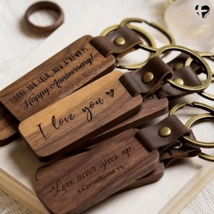 Wooden keychains with engraved messages, attached to gold rings, displayed on a white surface.
