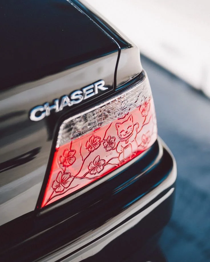 Close-up of the rear of a black car with a 'Chaser' badge and a red, floral, fox-themed sticker on the tail light.