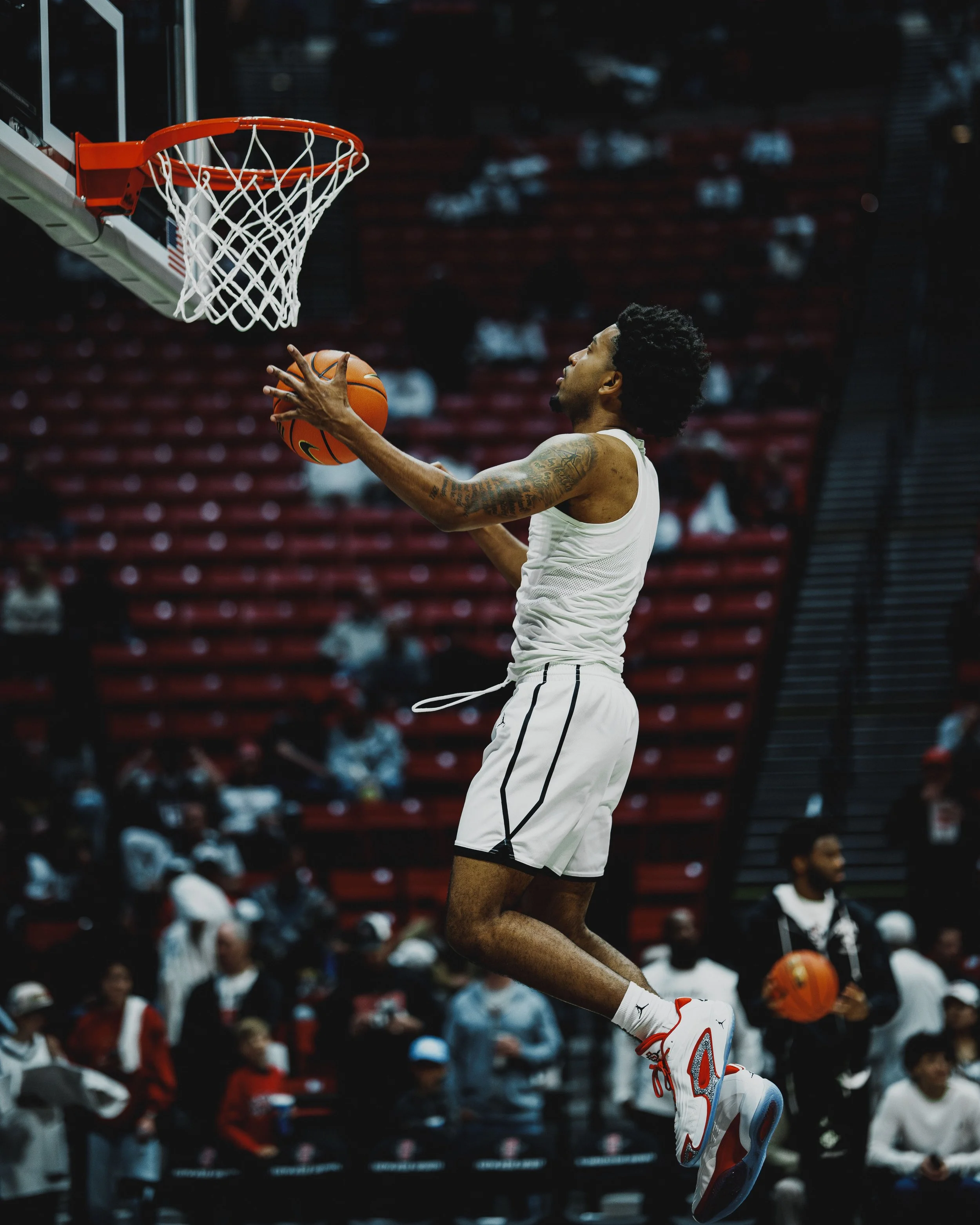 A basketball player in a white uniform is jumping to make a shot towards the hoop during a game.