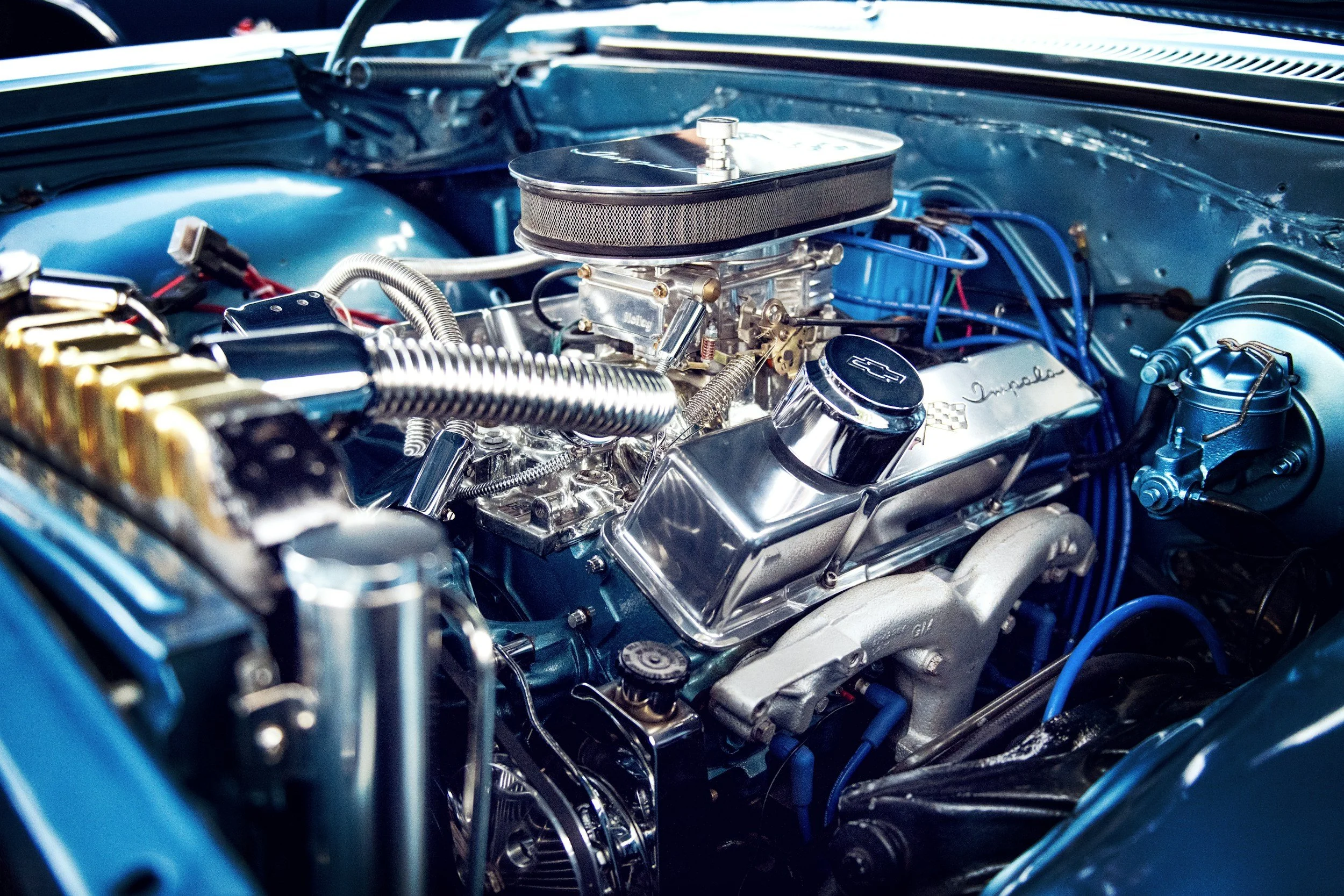 Close-up of a polished classic V8 car engine with chrome and metallic components, blue wiring, and a blue engine bay.