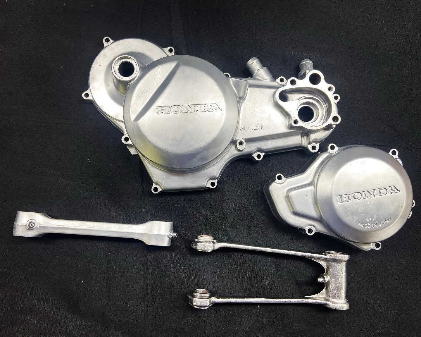 Two silver Honda motorcycle engine covers and two silver support brackets arranged on a black surface.