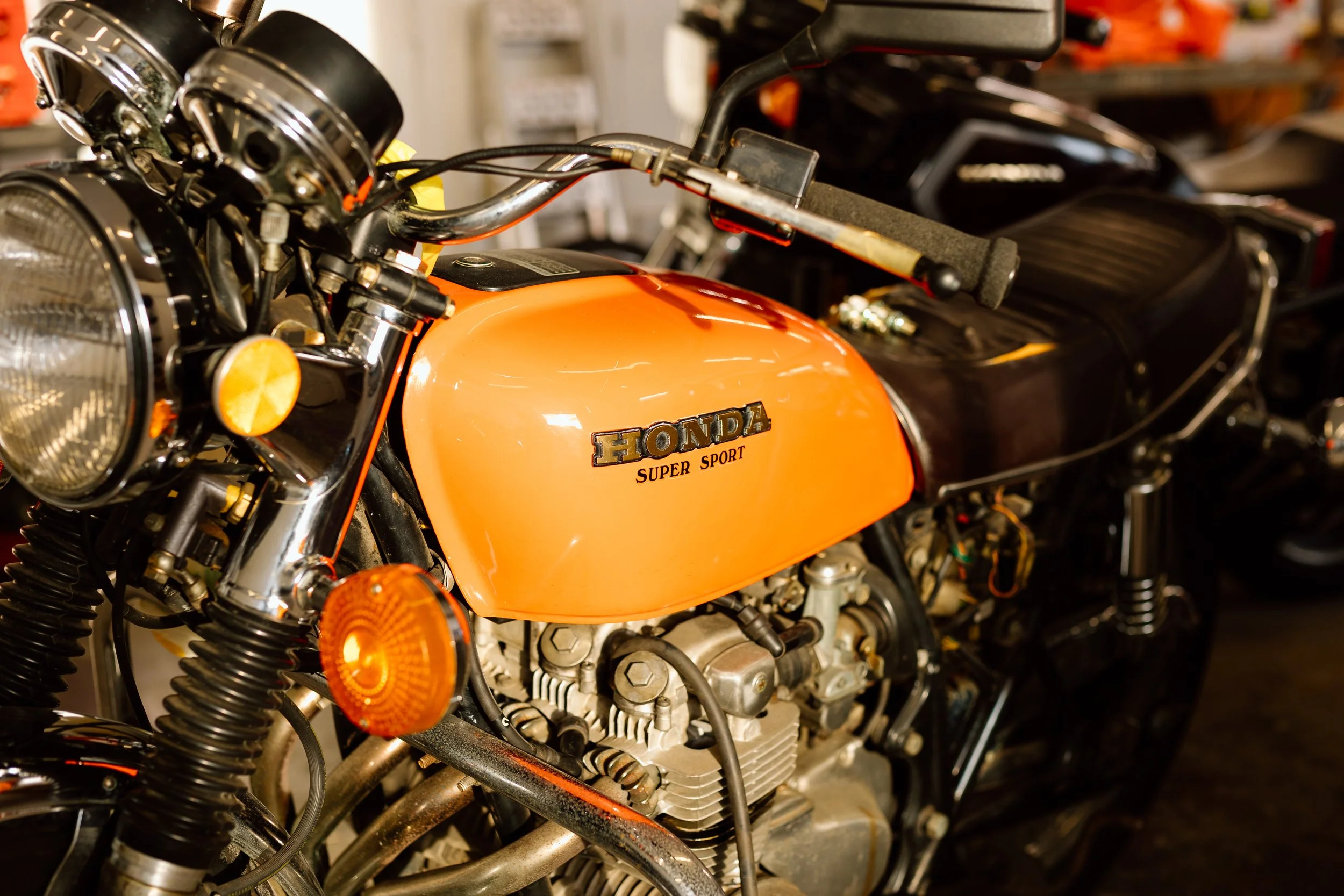 A vintage Honda Super Sport motorcycle with orange fuel tank and black seat, showing chrome handlebars, headlight, and front suspension.