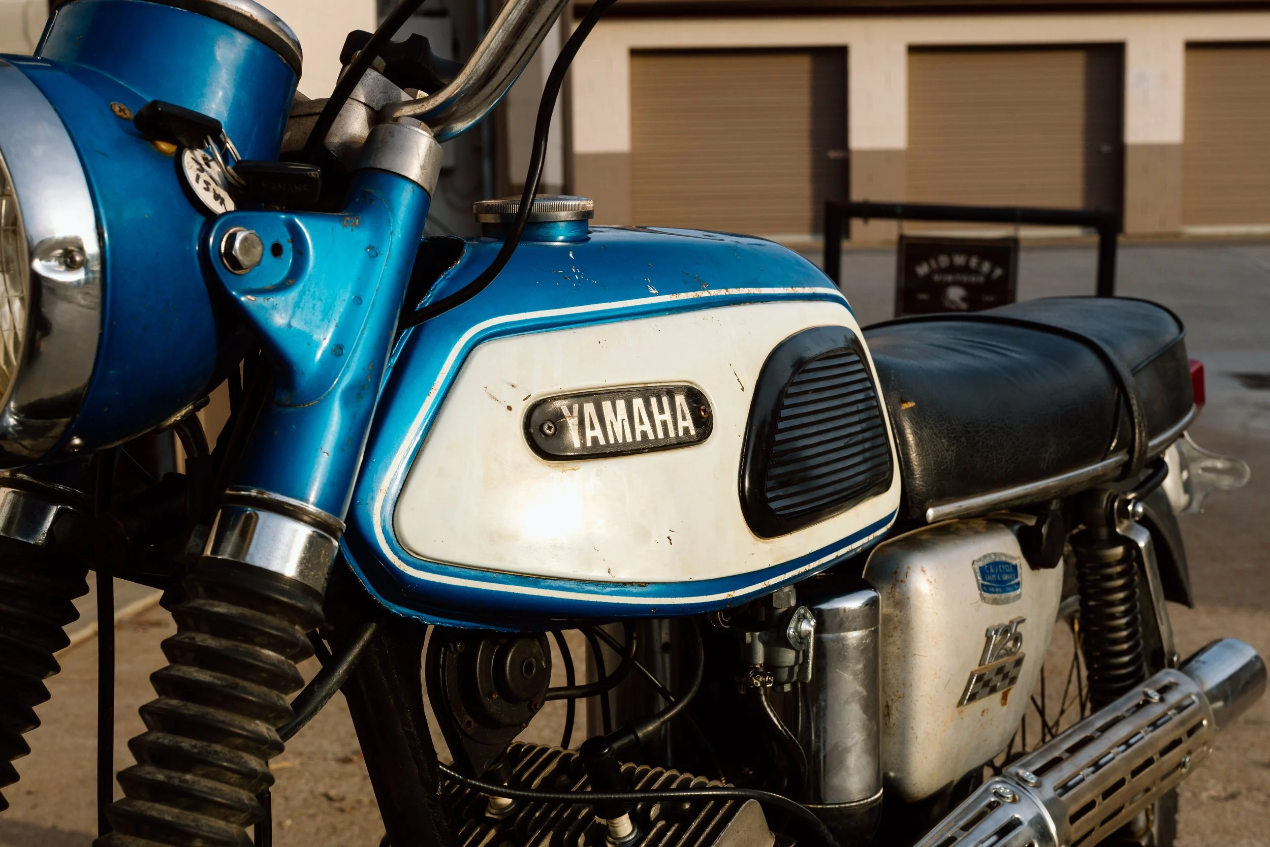 A vintage Yamaha motorcycle with a blue and white gas tank, black seat, and chrome accents, parked outdoors.