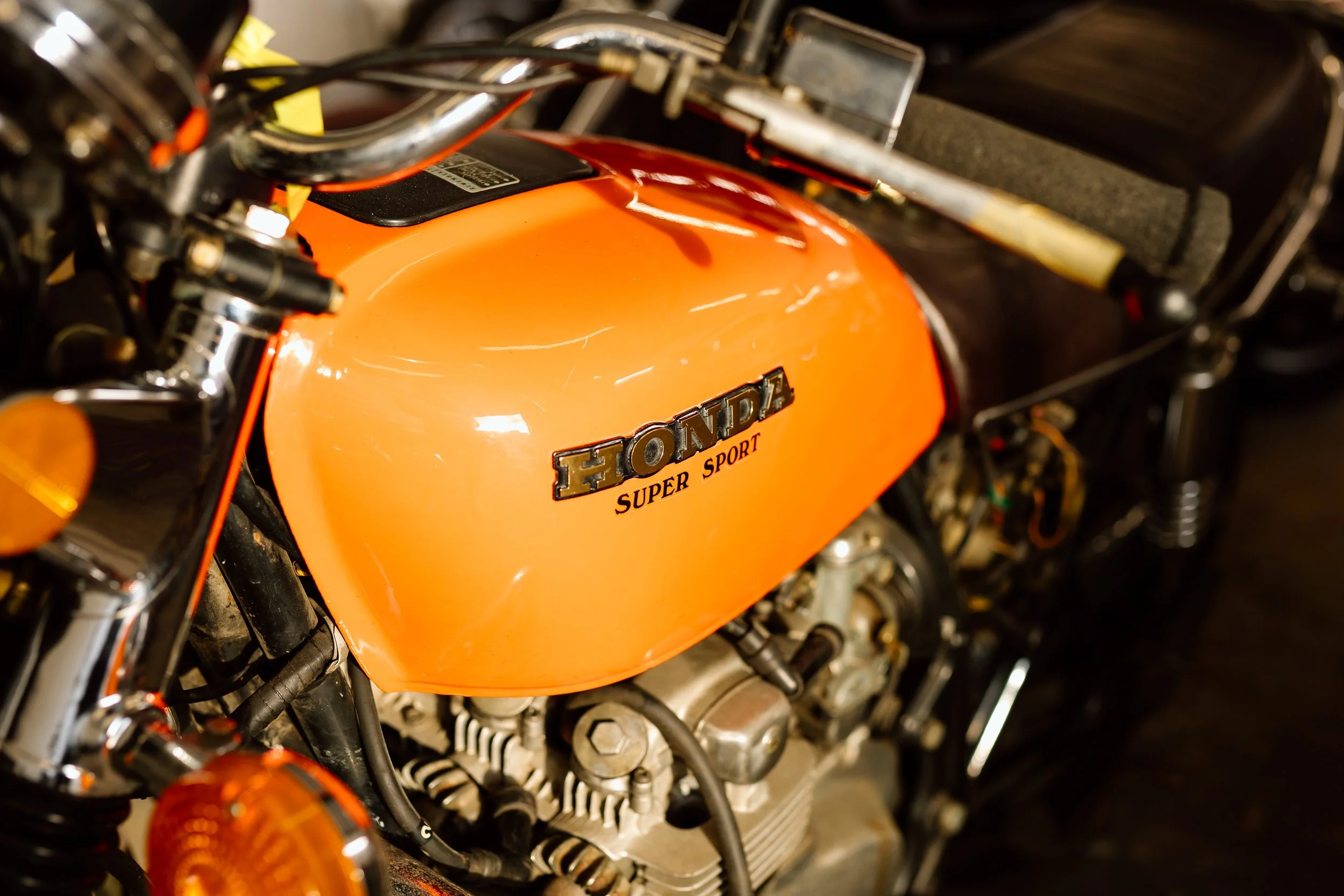 Close-up of a vintage orange Honda Super Sport motorcycle fuel tank with visible engine parts and handlebars.