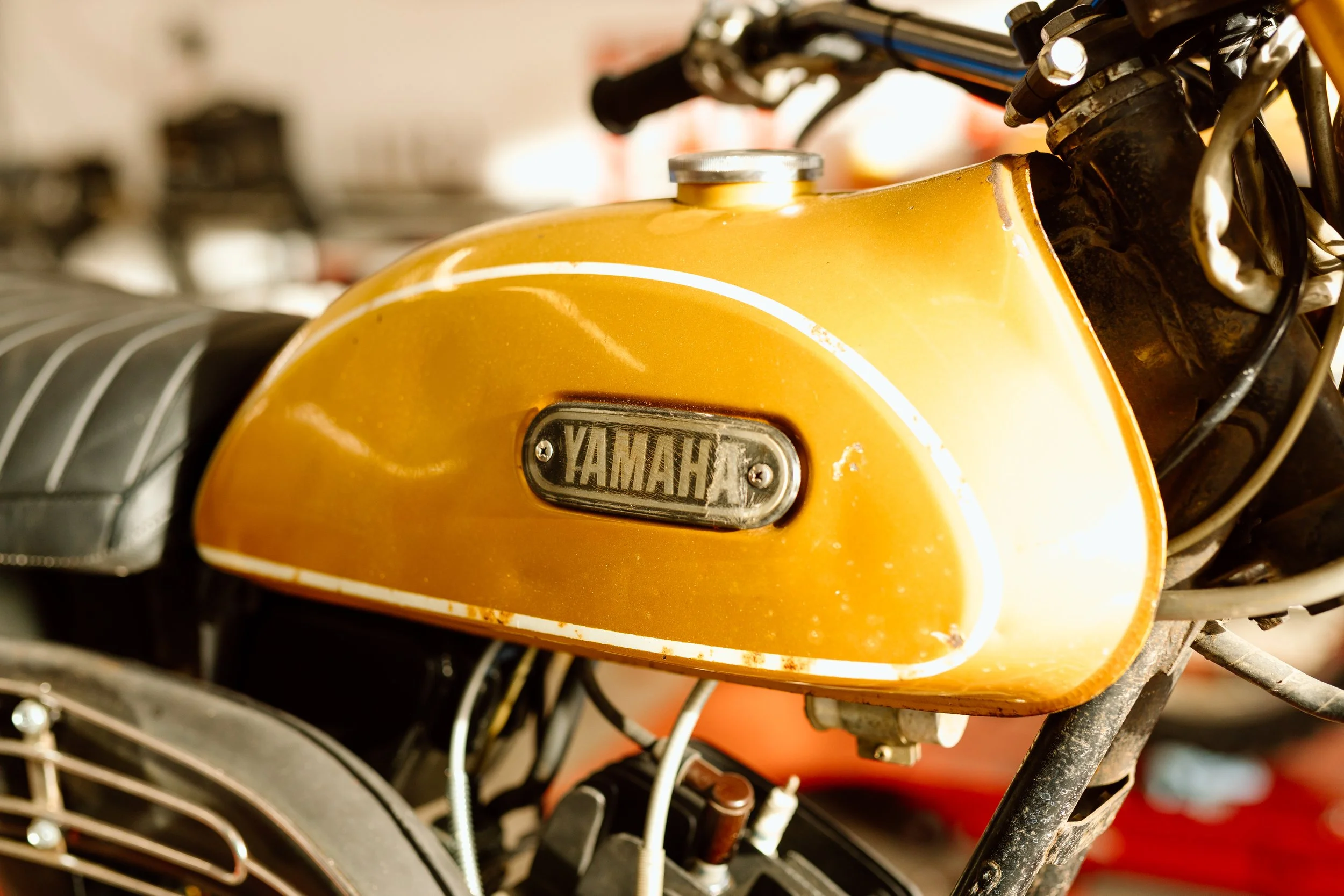 Close-up of a yellow Yamaha motorcycle gas tank with a Yamaha logo badge, showing signs of age and rust.