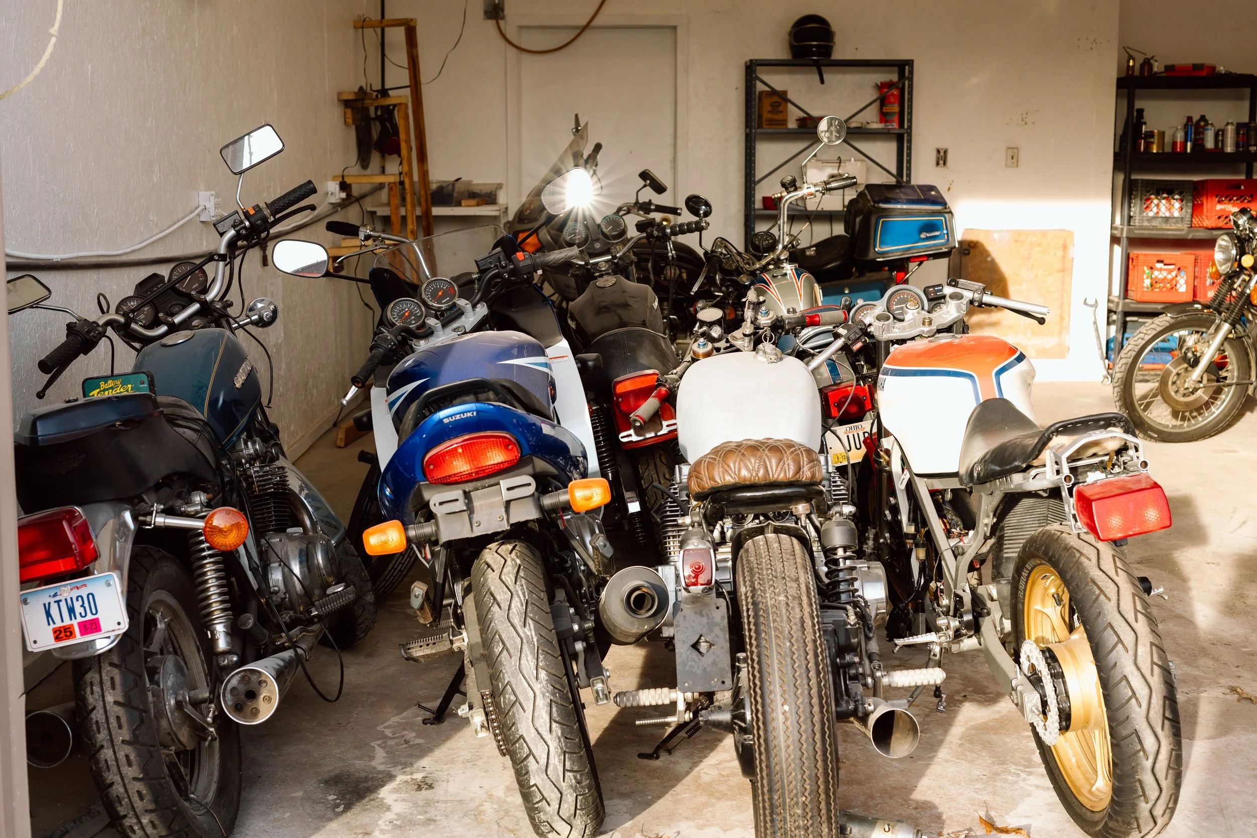 Several motorcycles and bikes parked in a garage, with shelves and tools in the background.