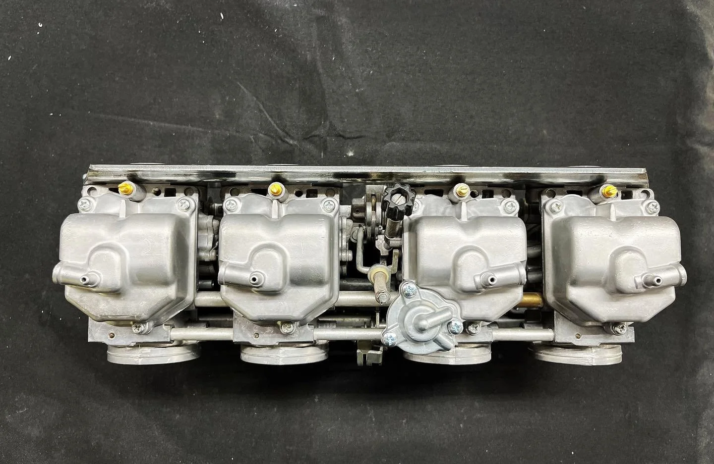 A silver intake manifold with four throttle bodies, placed on a black surface.