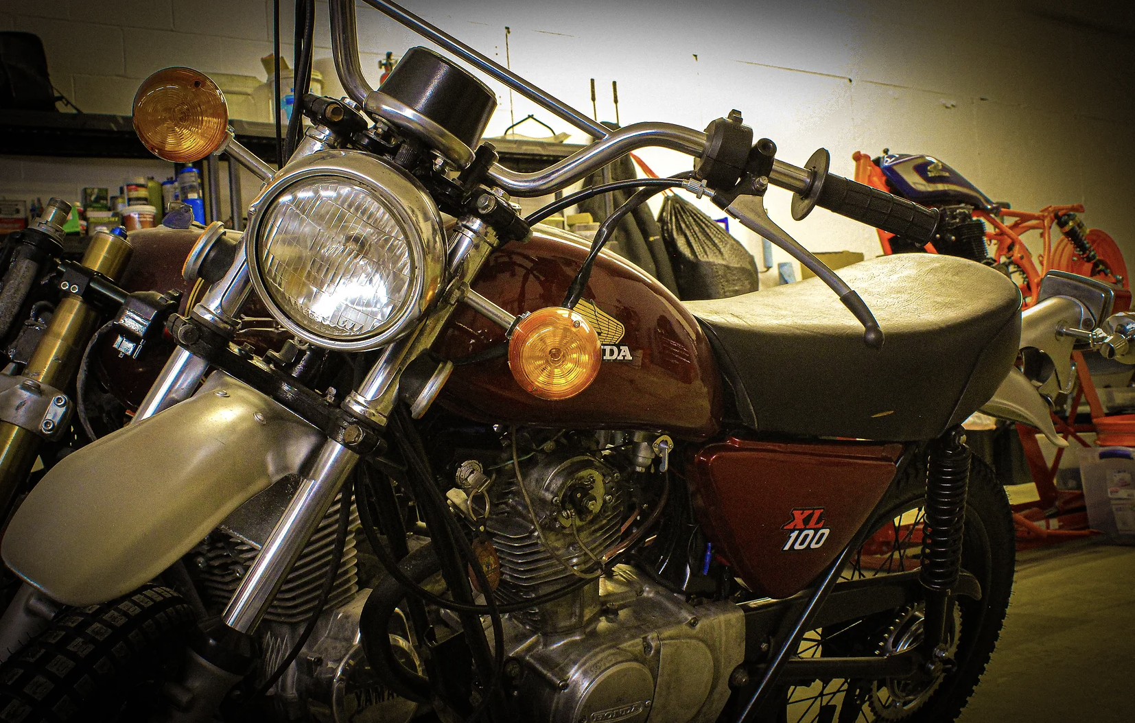 A vintage Honda XL 100 motorcycle in a garage, surrounded by tools and bike parts.