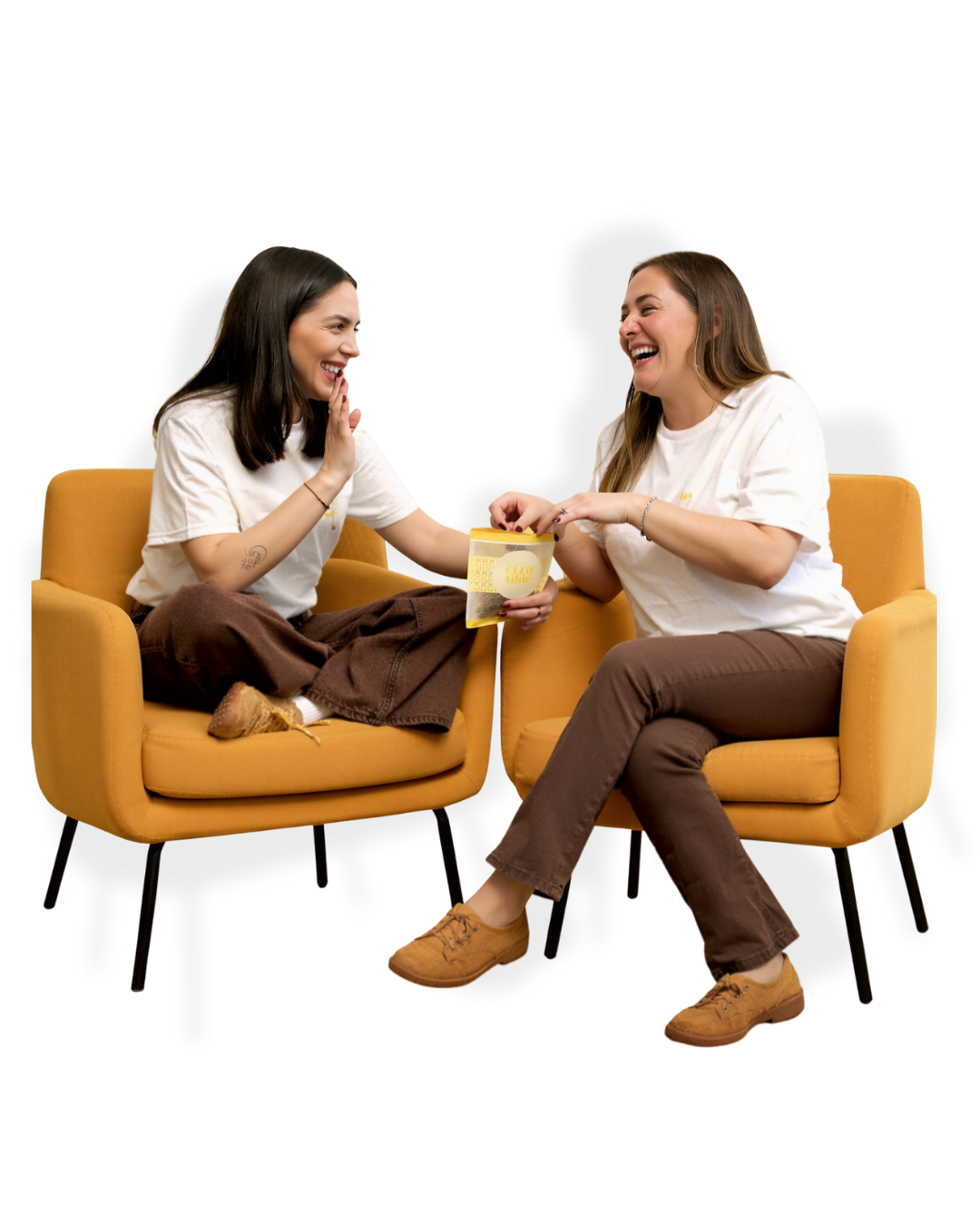 Two women sitting on orange chairs, smiling and sharing a moment, with one woman handing a yellow object to the other.