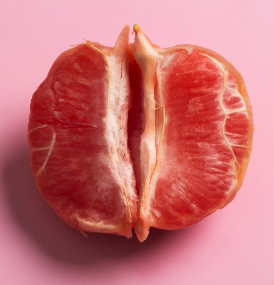 A peeled grapefruit with pink flesh on a pink background.