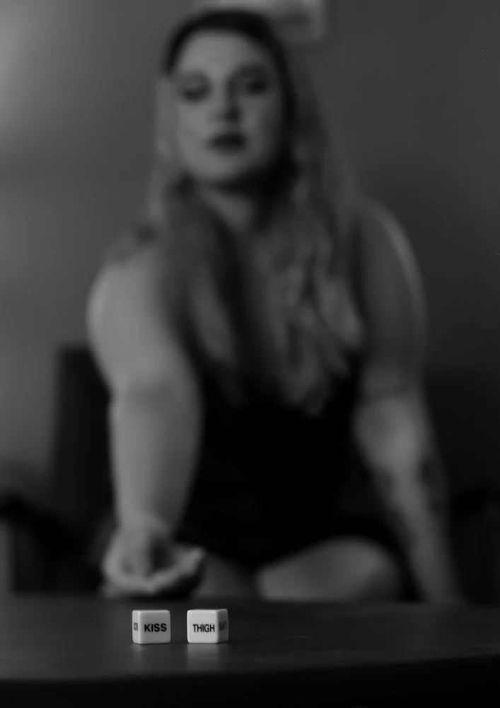Blurry woman sitting at a table with two dice in the foreground labeled 'KISS' and 'THIGH'.