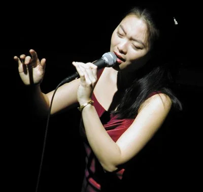 A woman singing passionately into a microphone on stage with closed eyes.