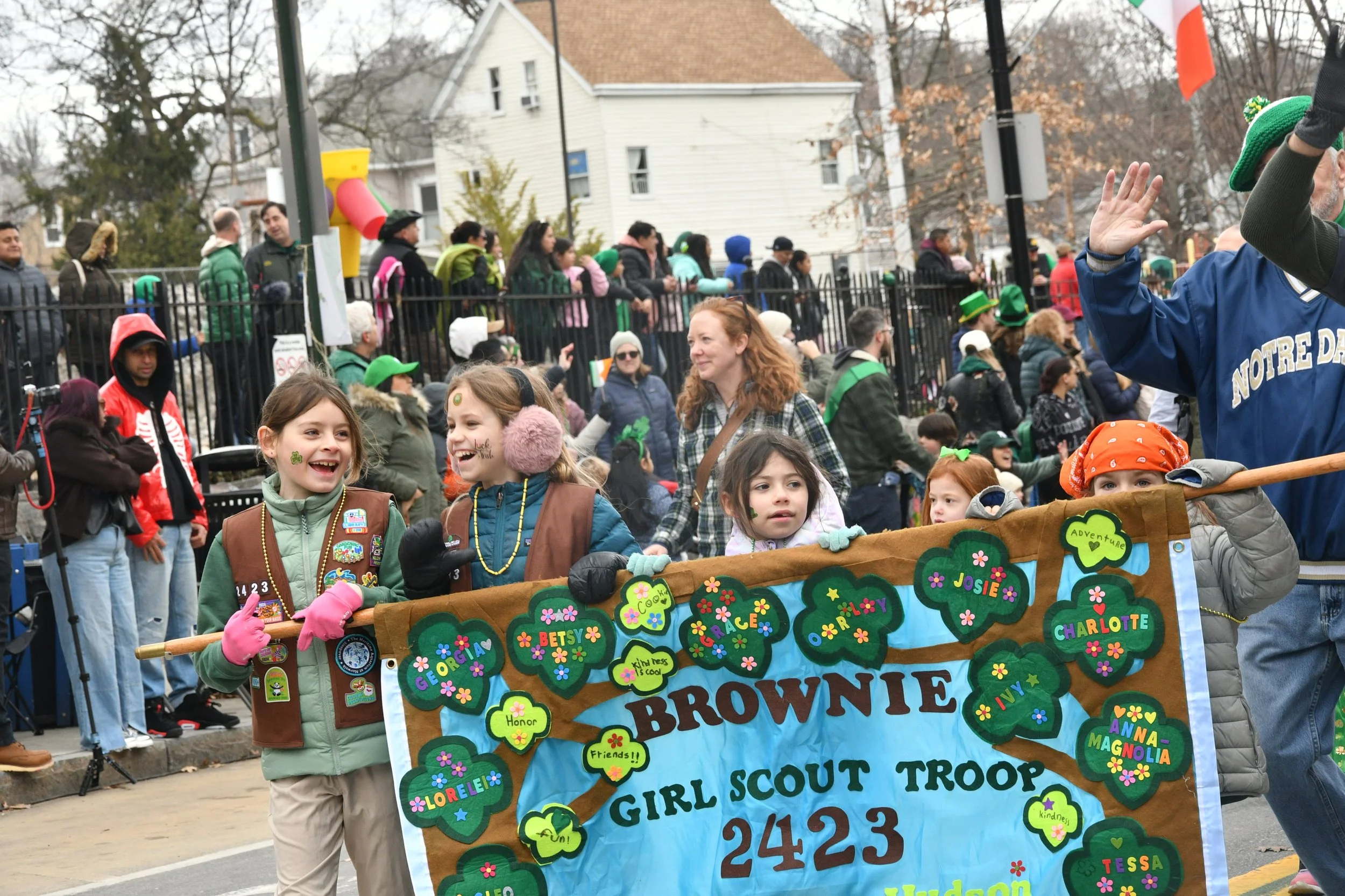 Children and adults participating in a parade, holding a colorful banner with various names and decorations, celebrating Girl Scout Troop 2423 during a fall event.