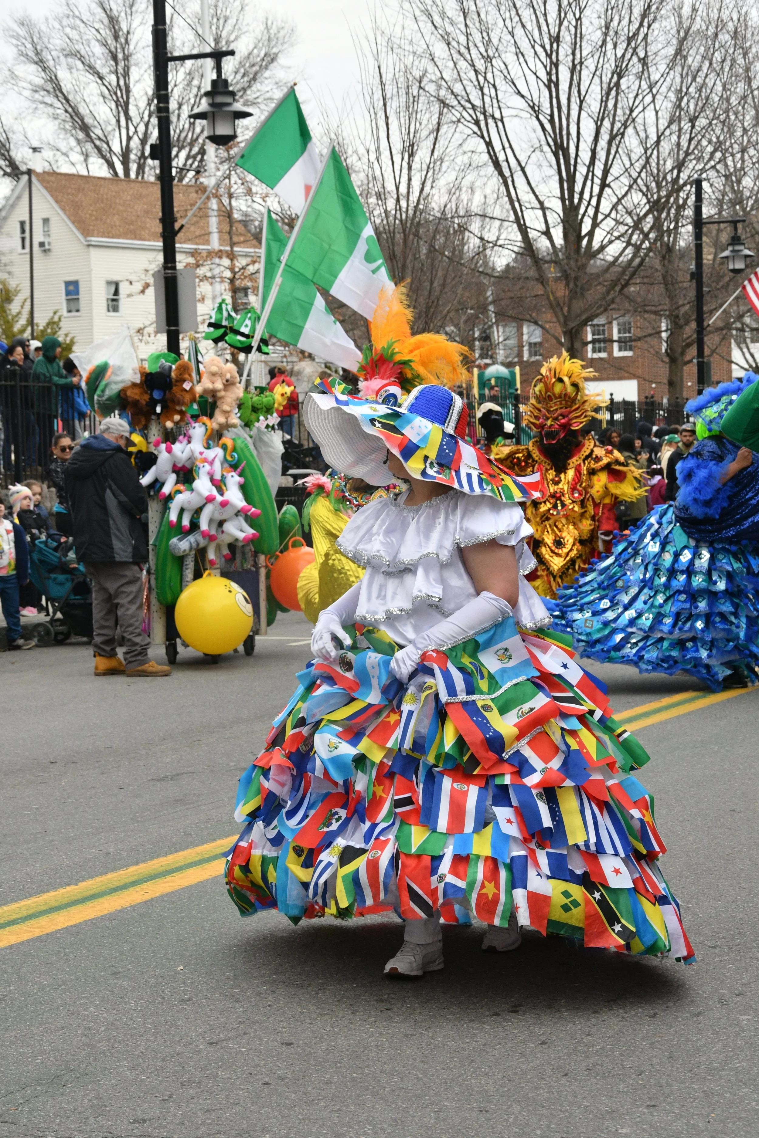 Person in colorful dress made of international flags, wearing a wide-brimmed hat and white gloves, participating in a parade or festival.