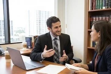 David Feingold and woman in a professional office setting having a discussion, with a laptop and books on the table.