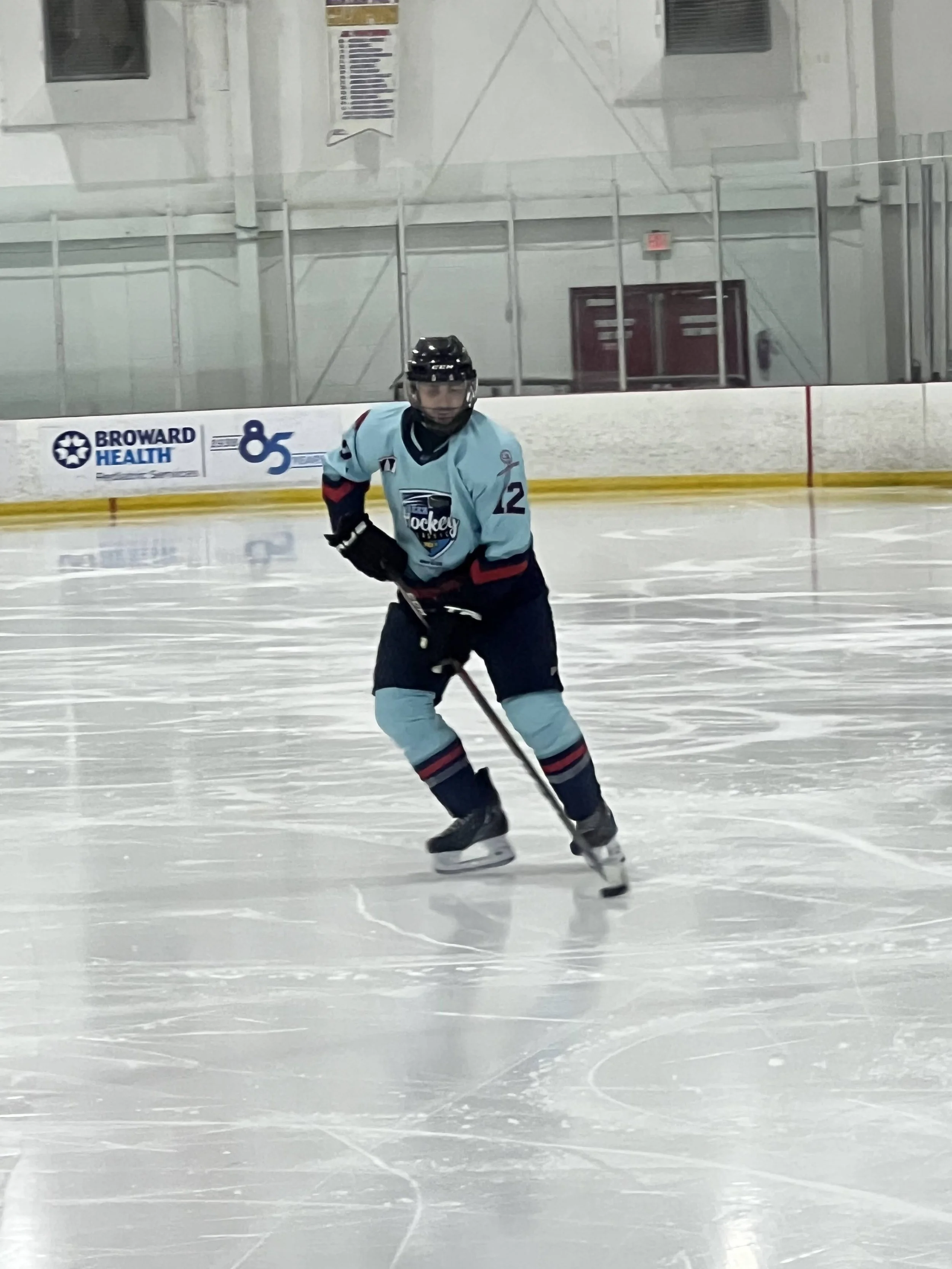David Feingold, employment attorney and founder of DZ Law, playing hockey in a light blue jersey and black helmet controlling the puck on the ice rink.