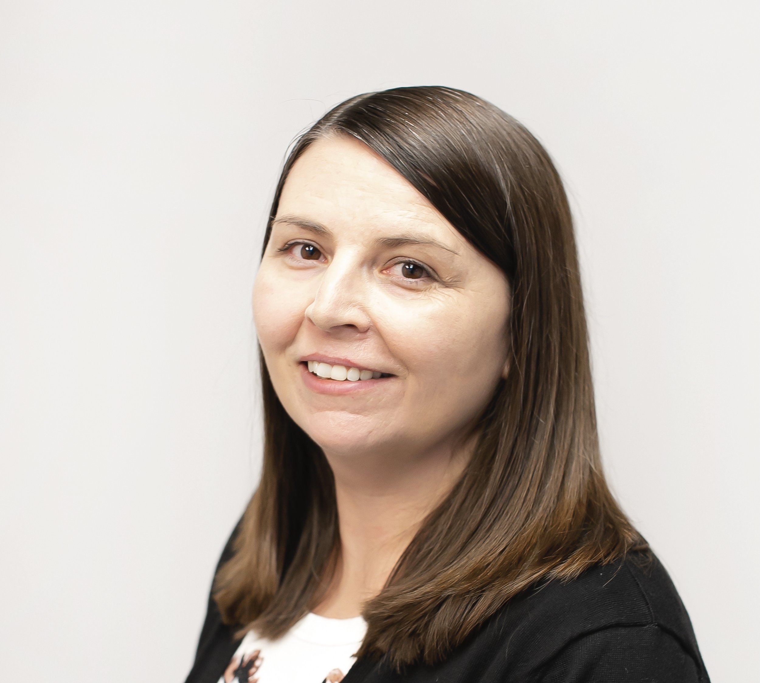 A woman with brown hair and brown eyes looking into the camera with a soft smile