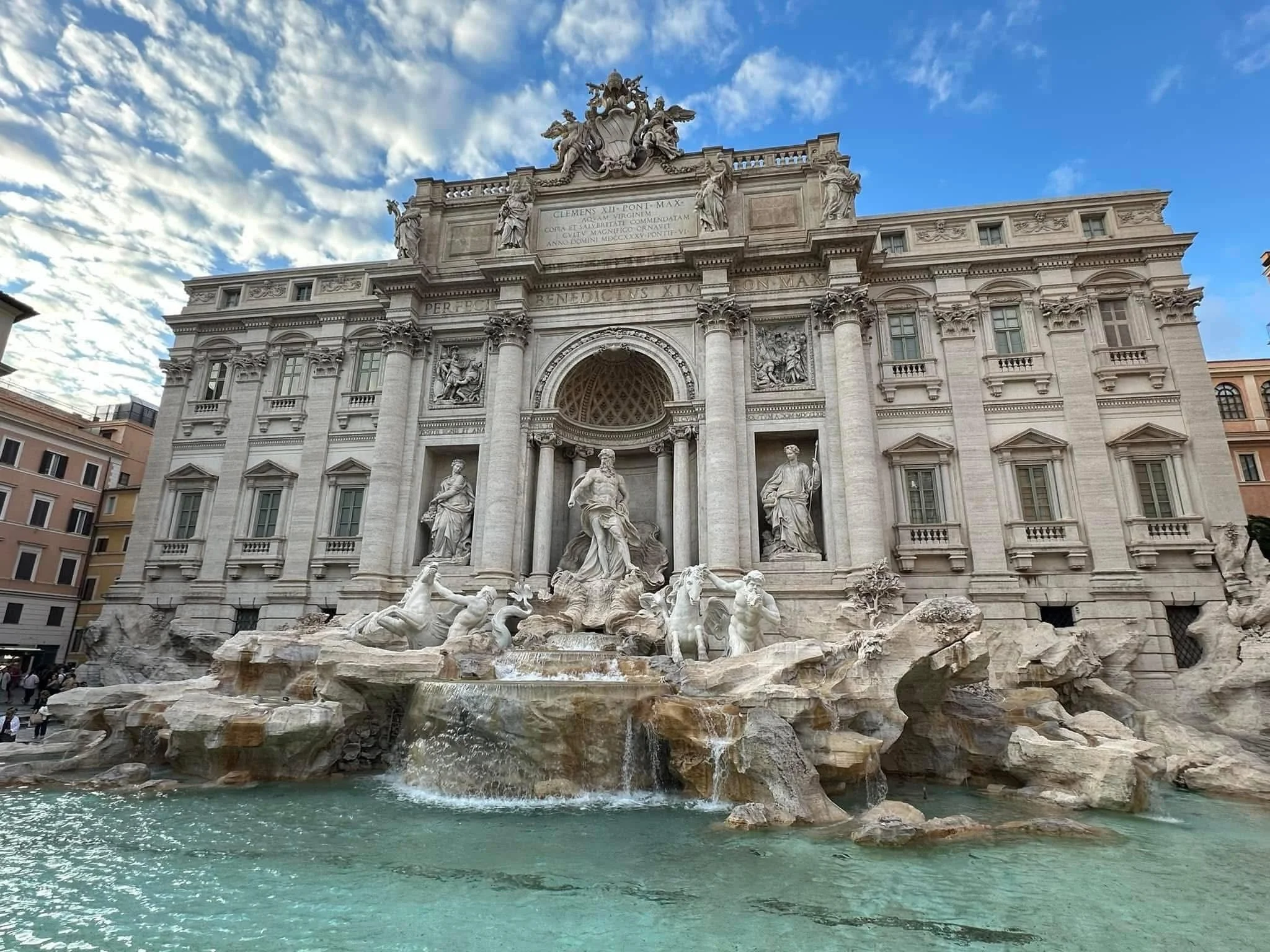 The Trevi Fountain in Rome, Italy, with detailed sculptures and cascading water at the base, under a blue sky with clouds.