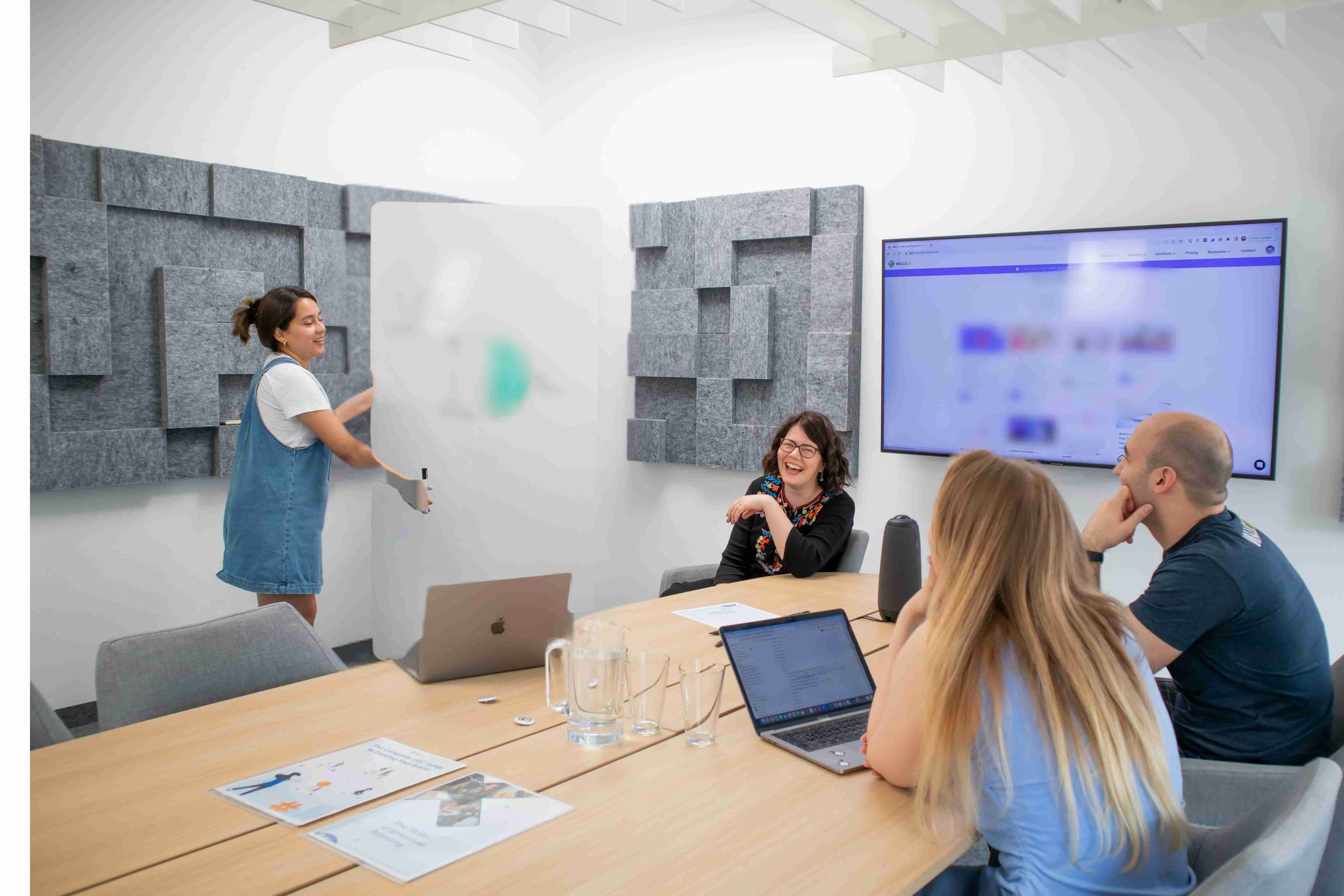 Three colleagues sit together in a conference room smiling as they partake in a course. There is a blurred screen behind them on the wall.