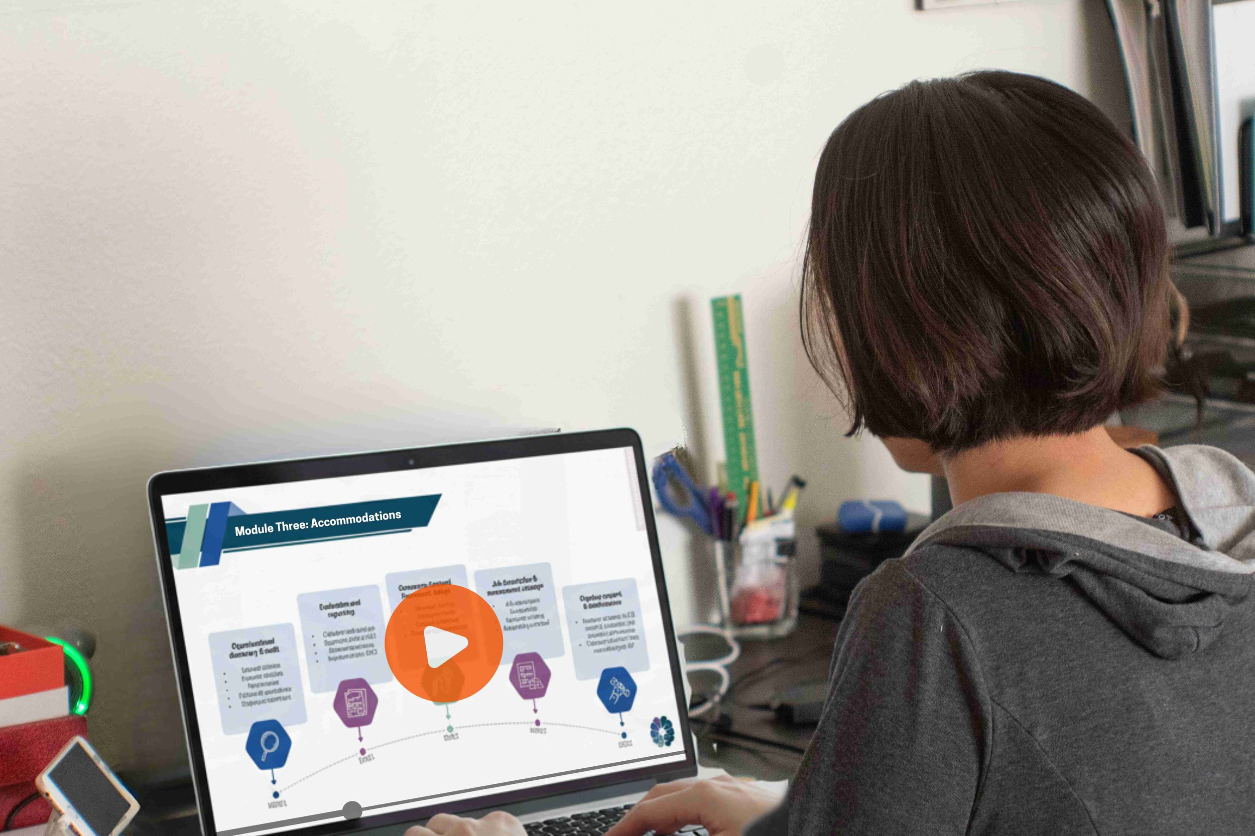 The camera is positioned behind a person wearing casual clothing who sits at a laptop. The point of view is over their shoulder and shows them watching an e-Learning module about accommodations on screen.