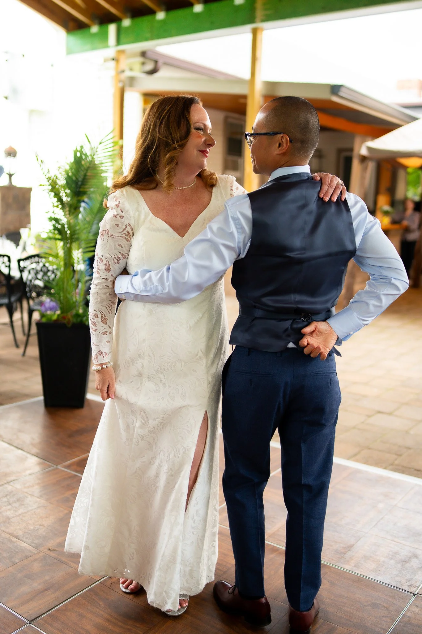 A woman in a white lace dress dancing with a man in a white shirt and dark vest at a wedding reception.