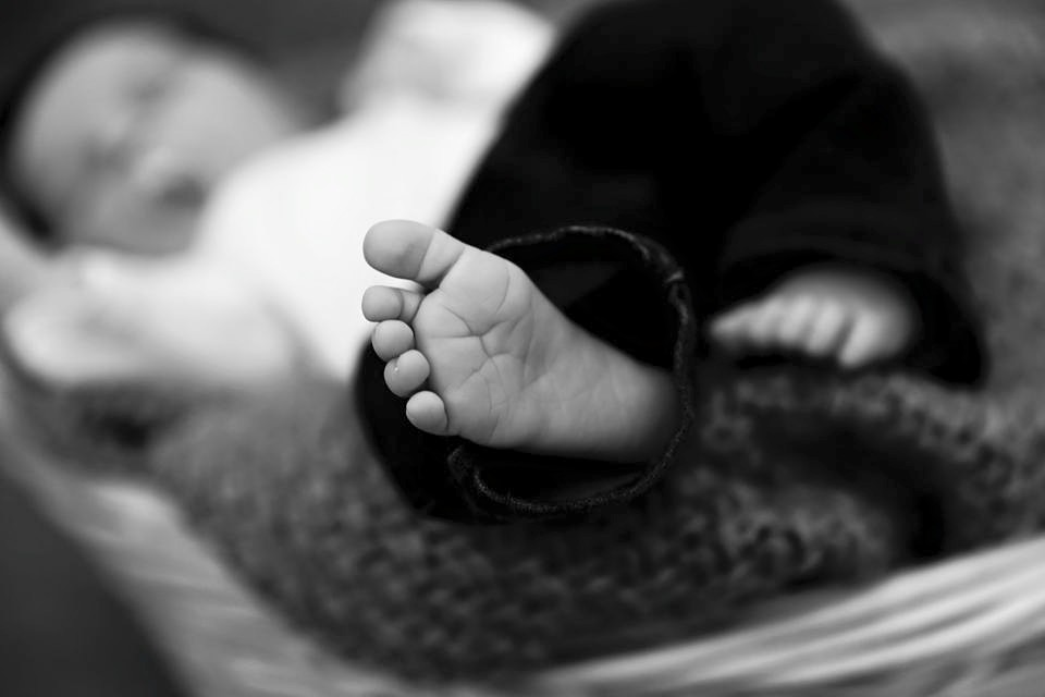 Close-up of a baby's hand gripping an adult's finger, with the baby lying on a blanket.