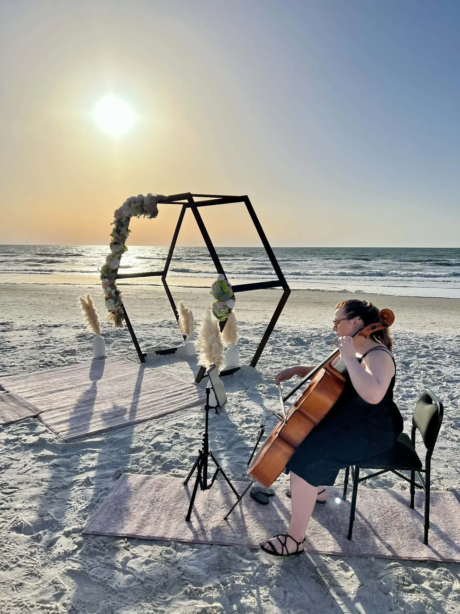 Carlyn playing for a beach wedding during sunset with a geometric frame decorated with flowers and pampas grass around it.