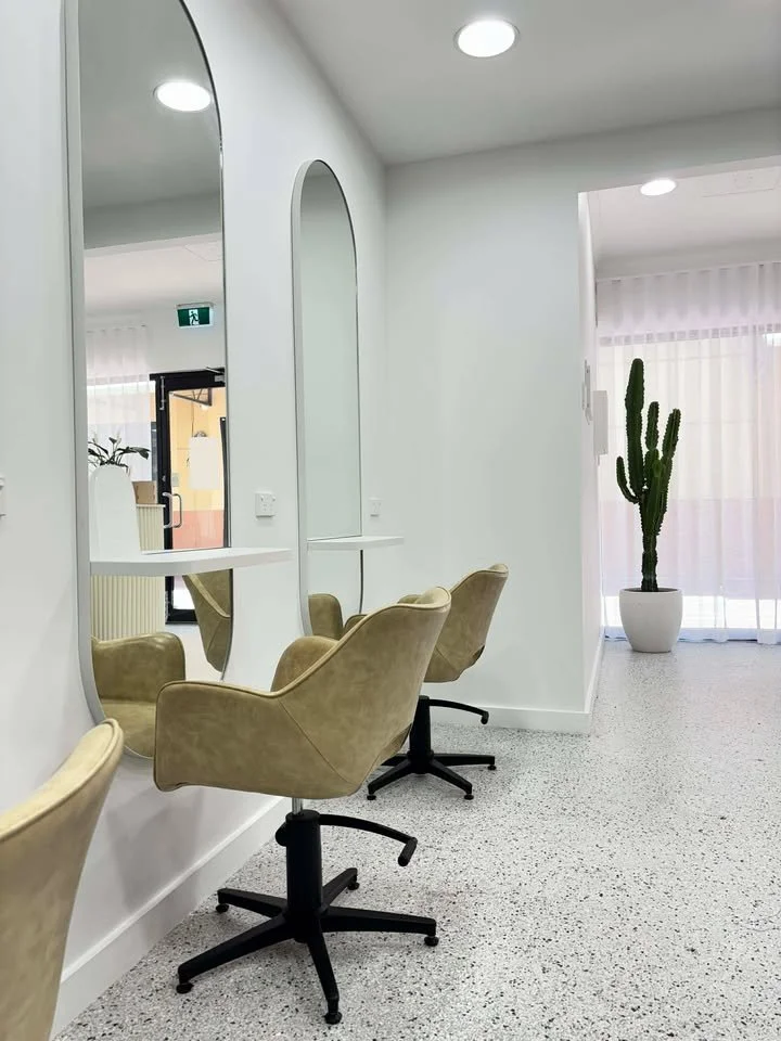 Hair salon with beige salon chairs in front of large mirrors on white walls and a tall cactus in a white pot in the corner.