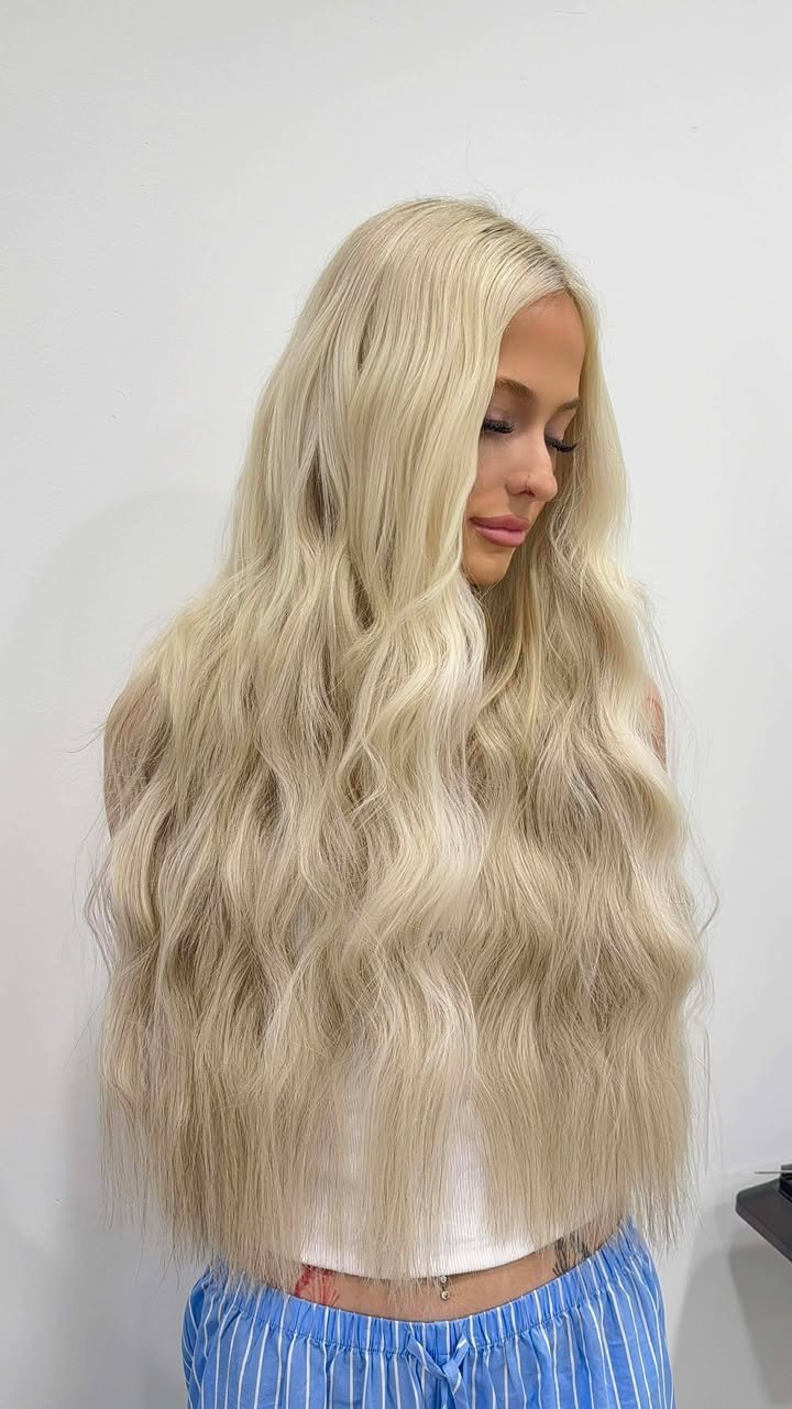 A woman with long, wavy blonde hair looking down against a plain white background.