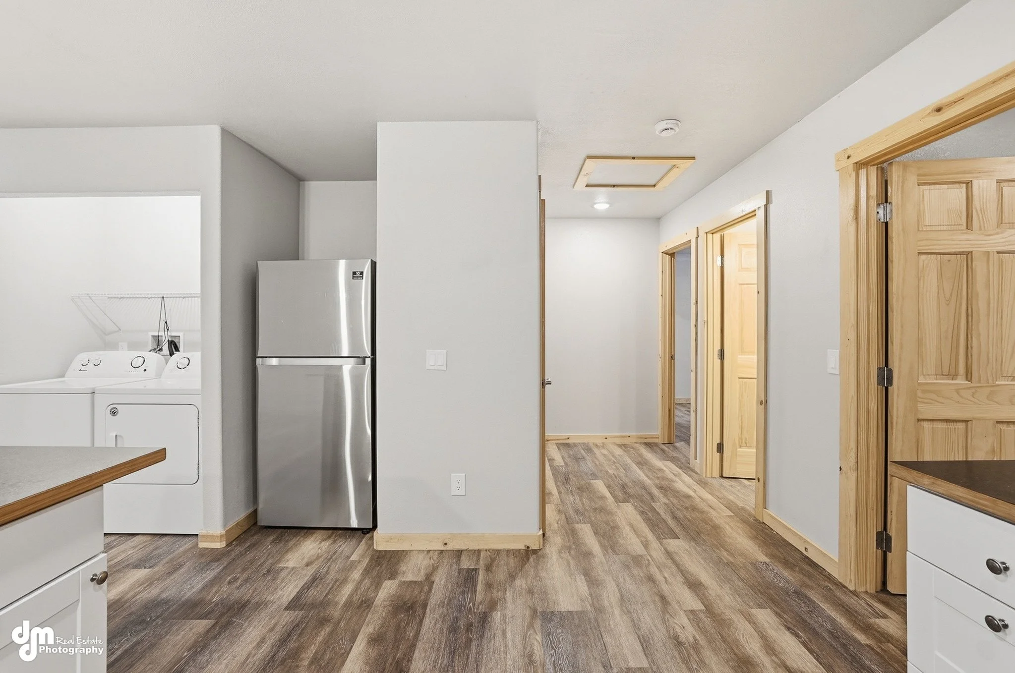 Interior of a house with white walls, wood trim, hardwood flooring, a white washer and dryer, and a stainless steel refrigerator. There are multiple doorways with wooden trim leading to other rooms.