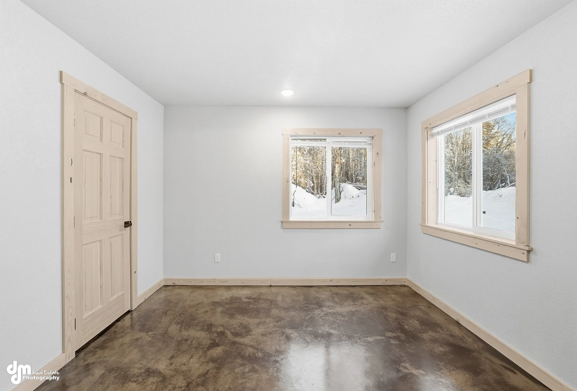 Empty room with white walls, wooden trim, and windows showing a snowy outdoor landscape.
