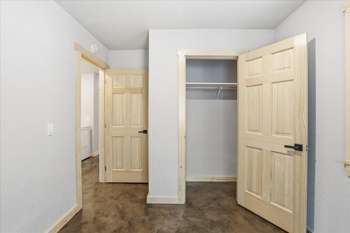 Empty room with a closet open showing a hanging rod, and two closed wooden doors, one leading to another room with a washer or dryer visible.