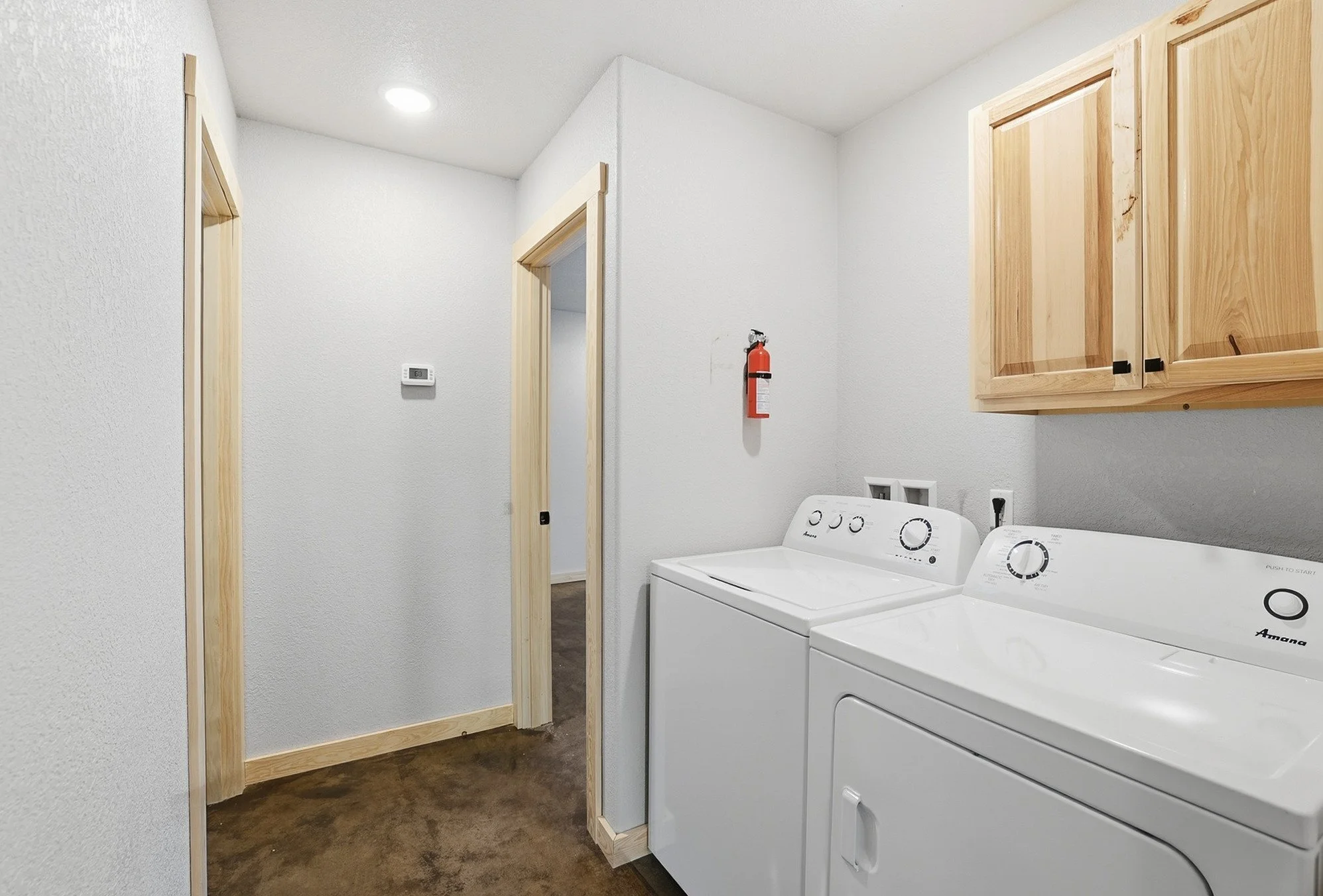 Laundry room with white washer and dryer, wooden cabinets, a fire extinguisher on the wall, and a thermostat.