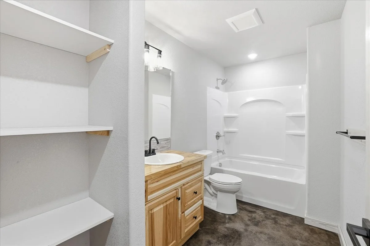 Bathroom with a wooden vanity with a sink, a mirror, a shower/tub combo with shelves, and white walls.