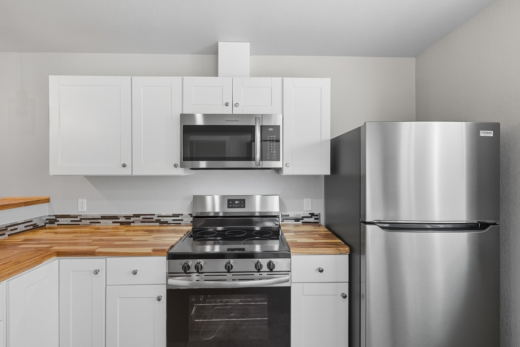Modern kitchen with white cabinets, a stainless steel microwave, oven, and refrigerator, and wooden countertops.