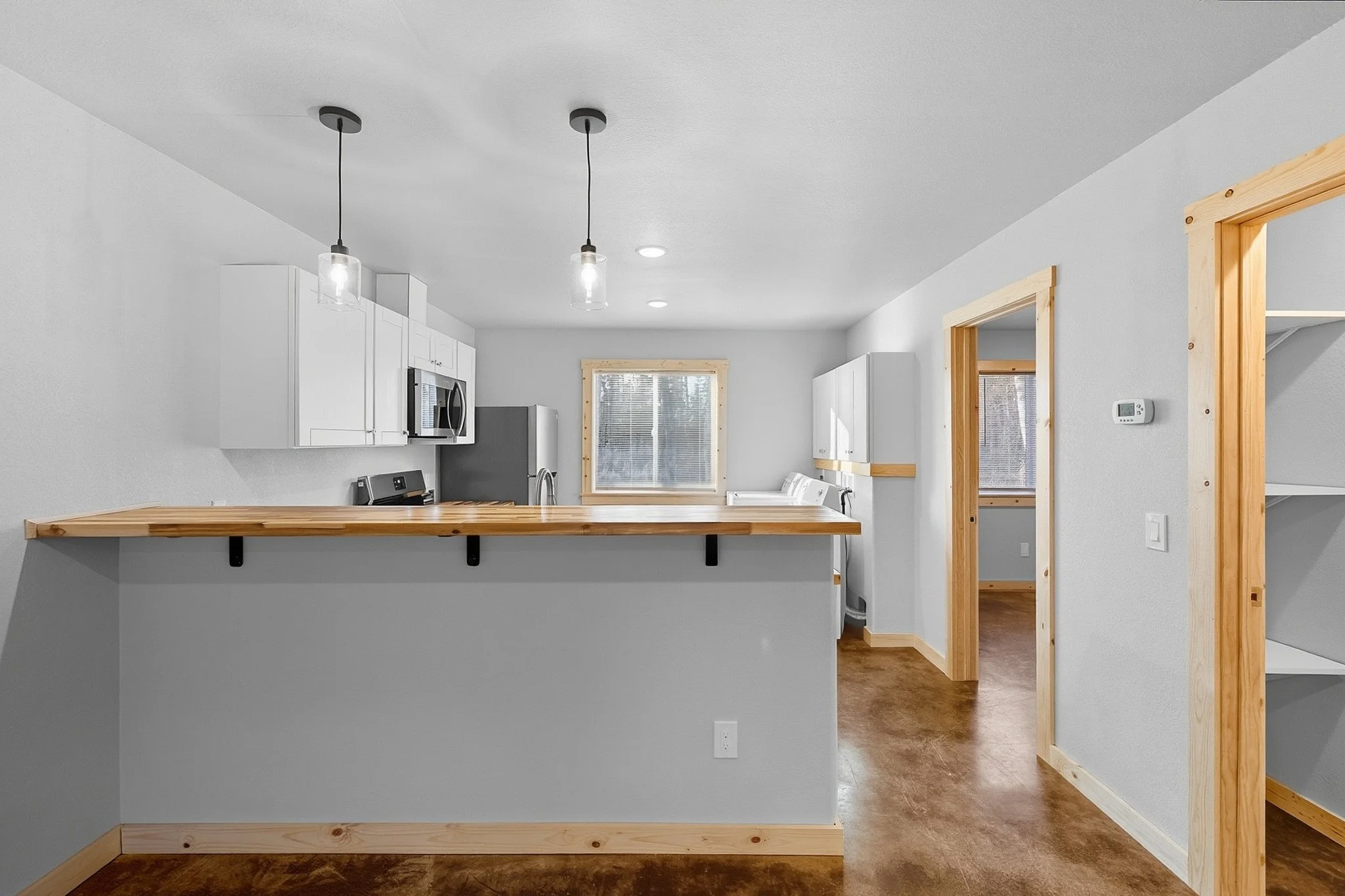 Kitchen with white cabinets, stainless steel appliances, wooden accents, and a window, viewed from a small breakfast bar or counter with two hanging pendant lights.